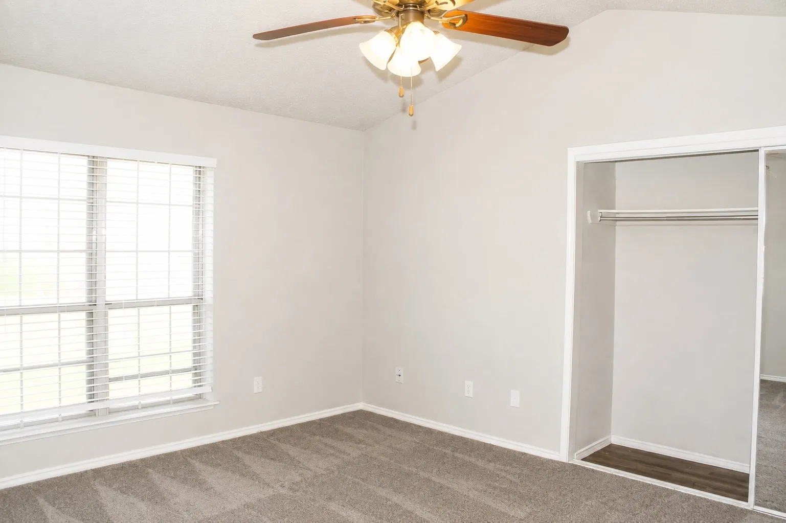 Vaulted ceiling, ceiling fan with integrated lighting, window with horizontal blinds, built-in closet with sliding mirrored doors, and carpet flooring