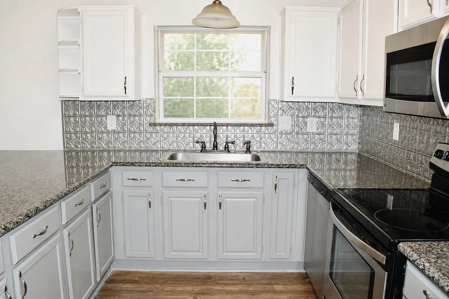 U-shaped kitchen featuring granite-look countertops, stainless steel appliances, a tin-look backsplash, and wood-finish flooring