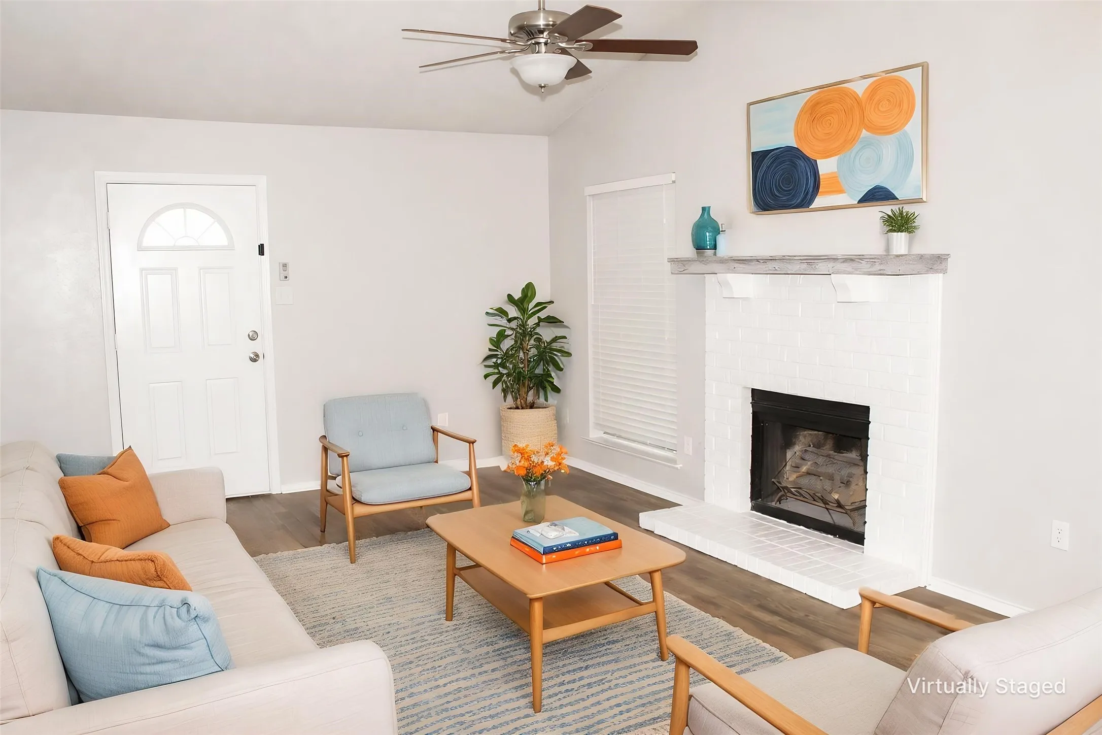 Vaulted ceiling with a ceiling fan, wood-finish flooring, white brick fireplace with a mantel, and a paneled entry door with an arched window