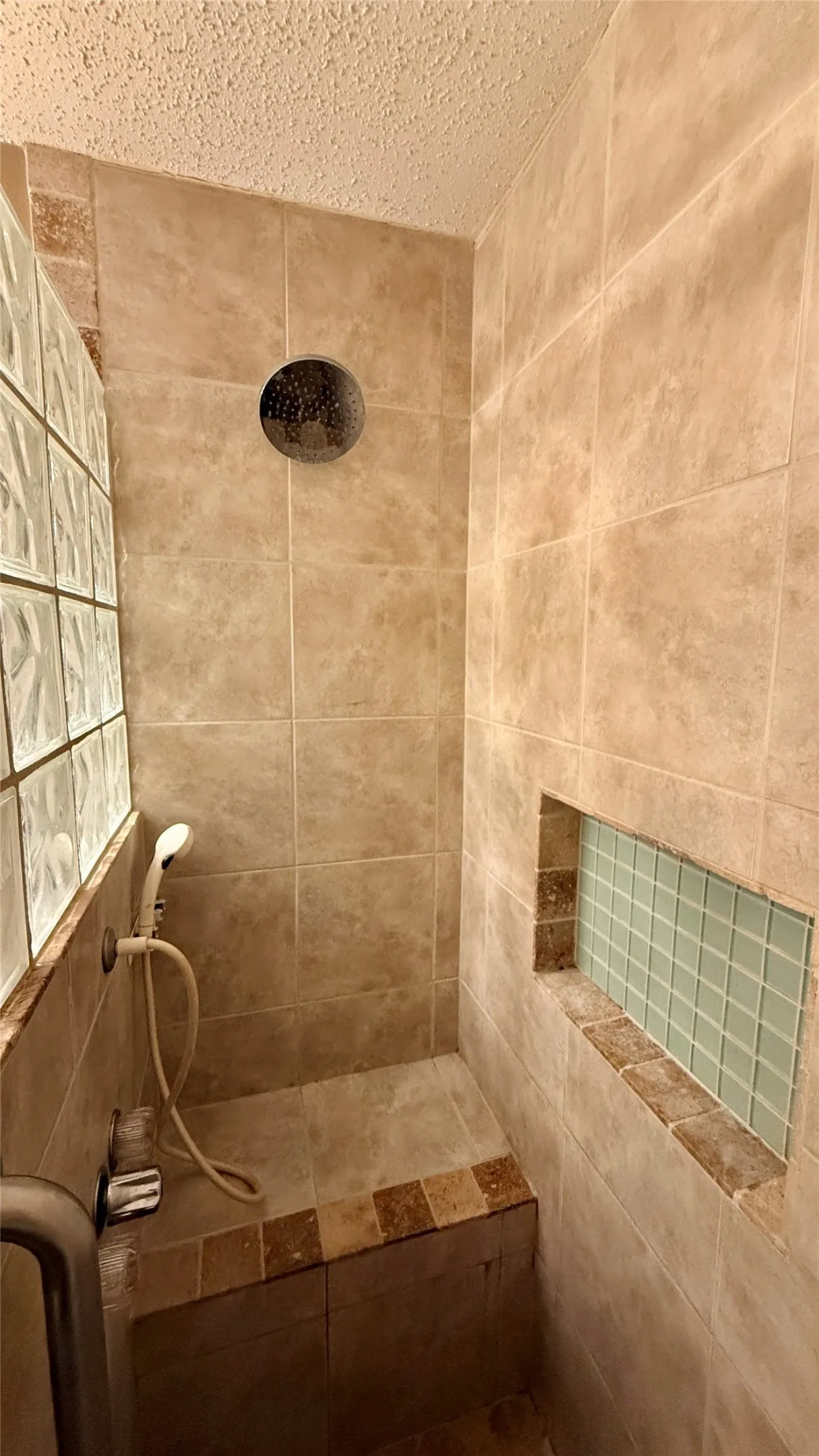 Tiled shower enclosure featuring a built-in bench, recessed niche with mosaic tile, glass block wall, and a rainfall showerhead with a handheld sprayer