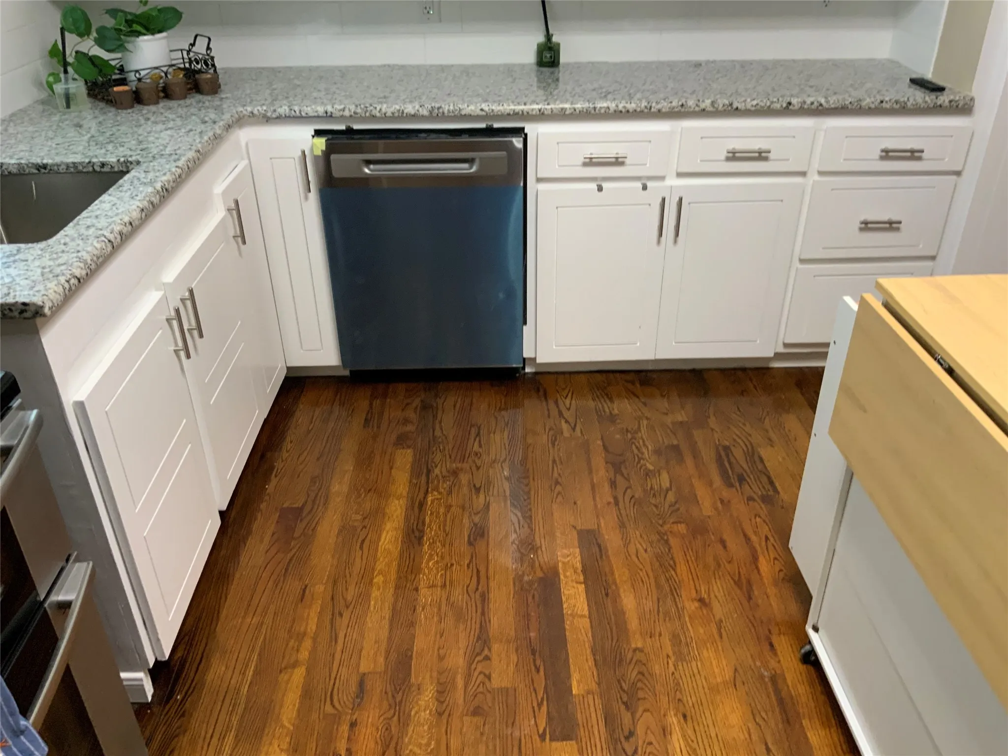 Kitchen featuring wood-finish flooring, white cabinetry, integrated stainless steel dishwasher, and light-toned countertops