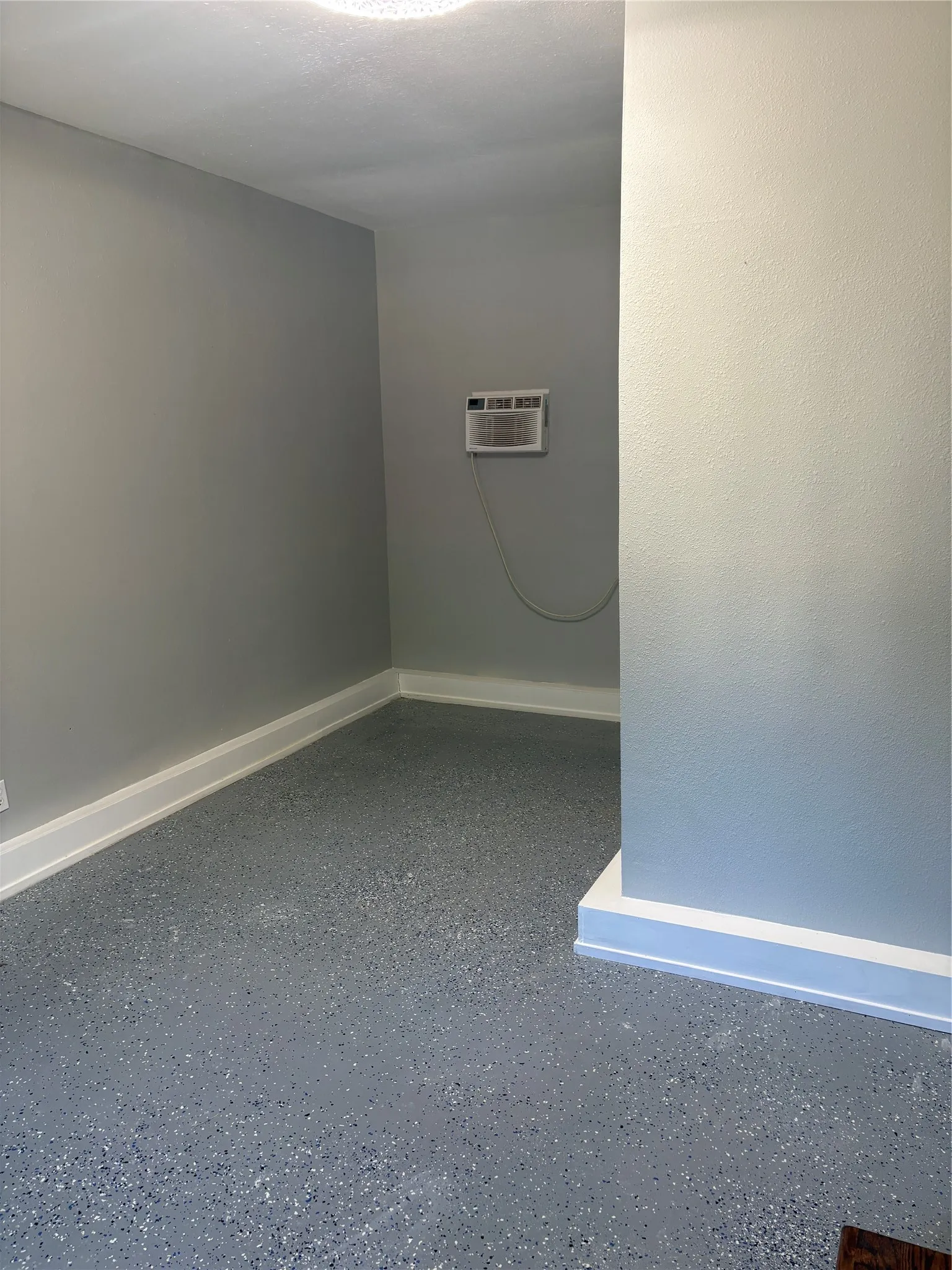 Neutral gray wall paint, textured flooring, white trim, and a wall-mounted AC unit