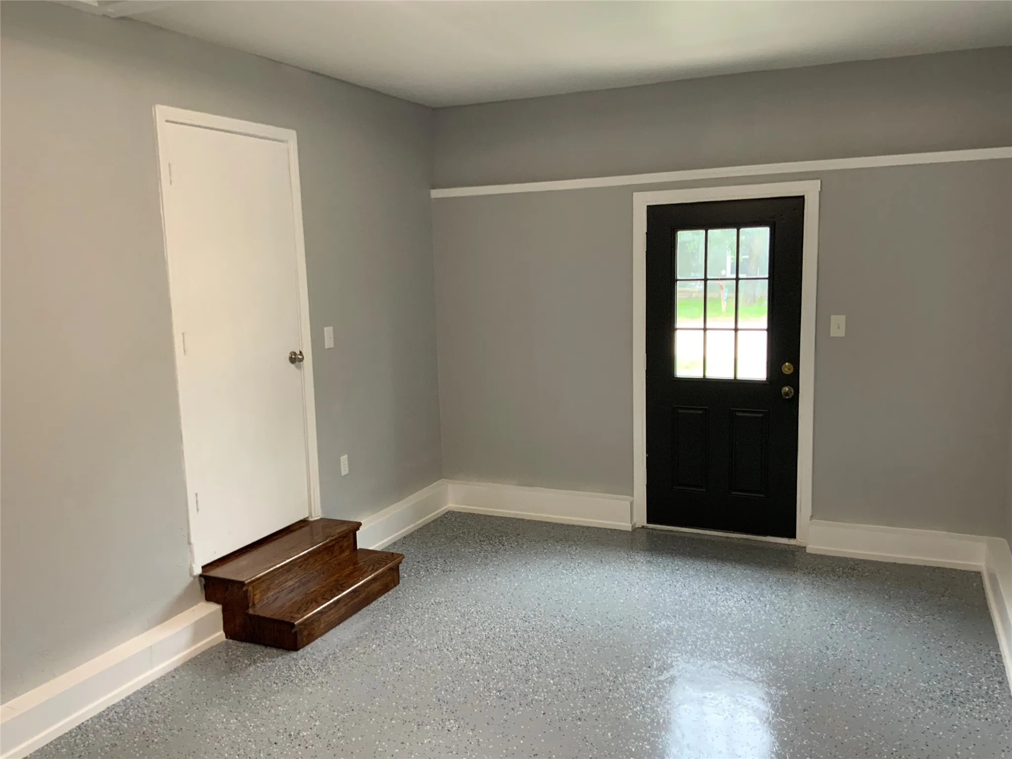 Interior space featuring light gray walls, white trim, and a gray speckled floor coating