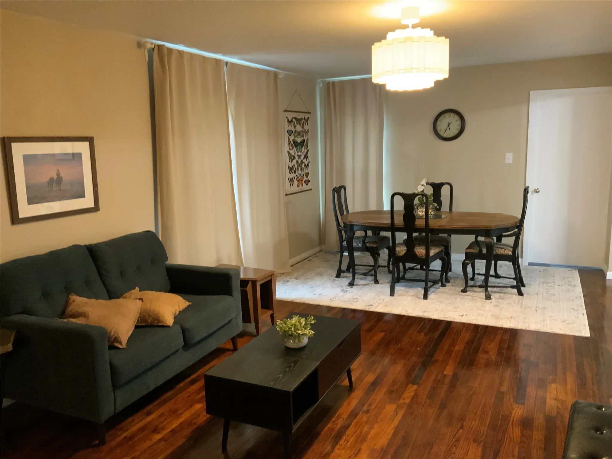 Open-concept living and dining area featuring rich wood-finish flooring, neutral paint palette, and a classic drum chandelier