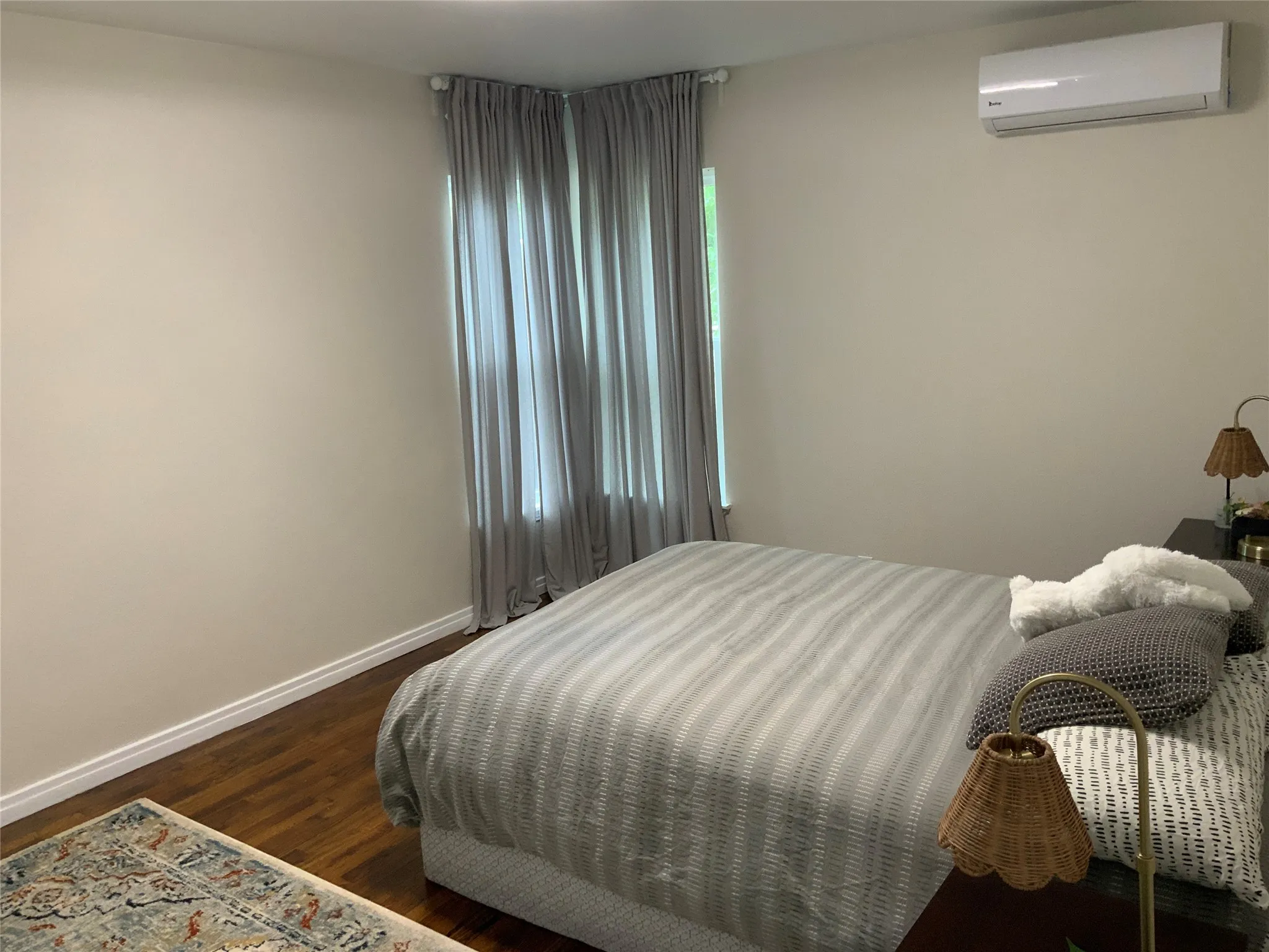 Bedroom featuring wood-finish flooring, light-toned walls, white baseboards, and a wall-mounted air conditioning unit