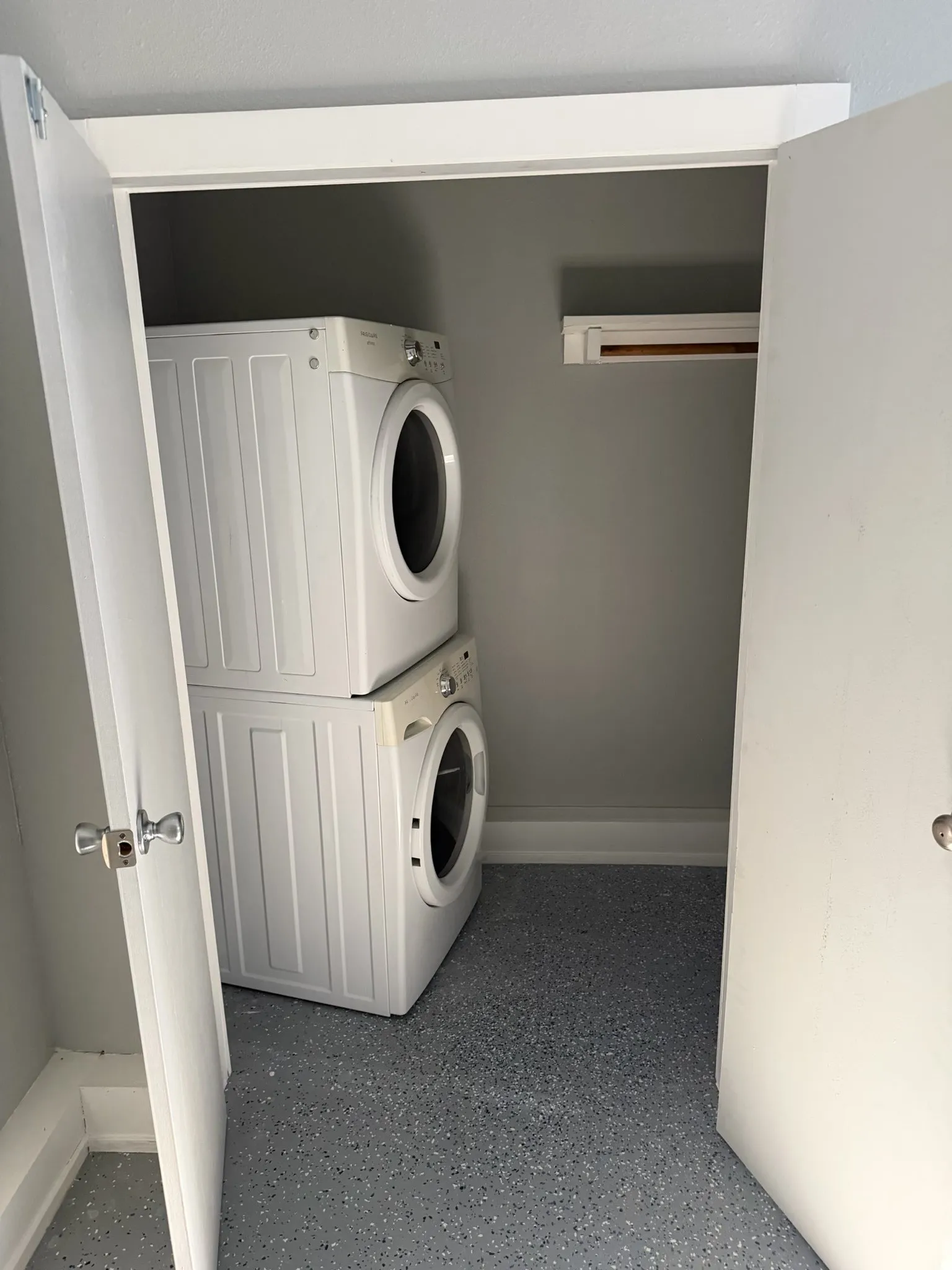 Laundry closet with a stackable washer and dryer, speckled epoxy flooring, and a built-in hanging rod