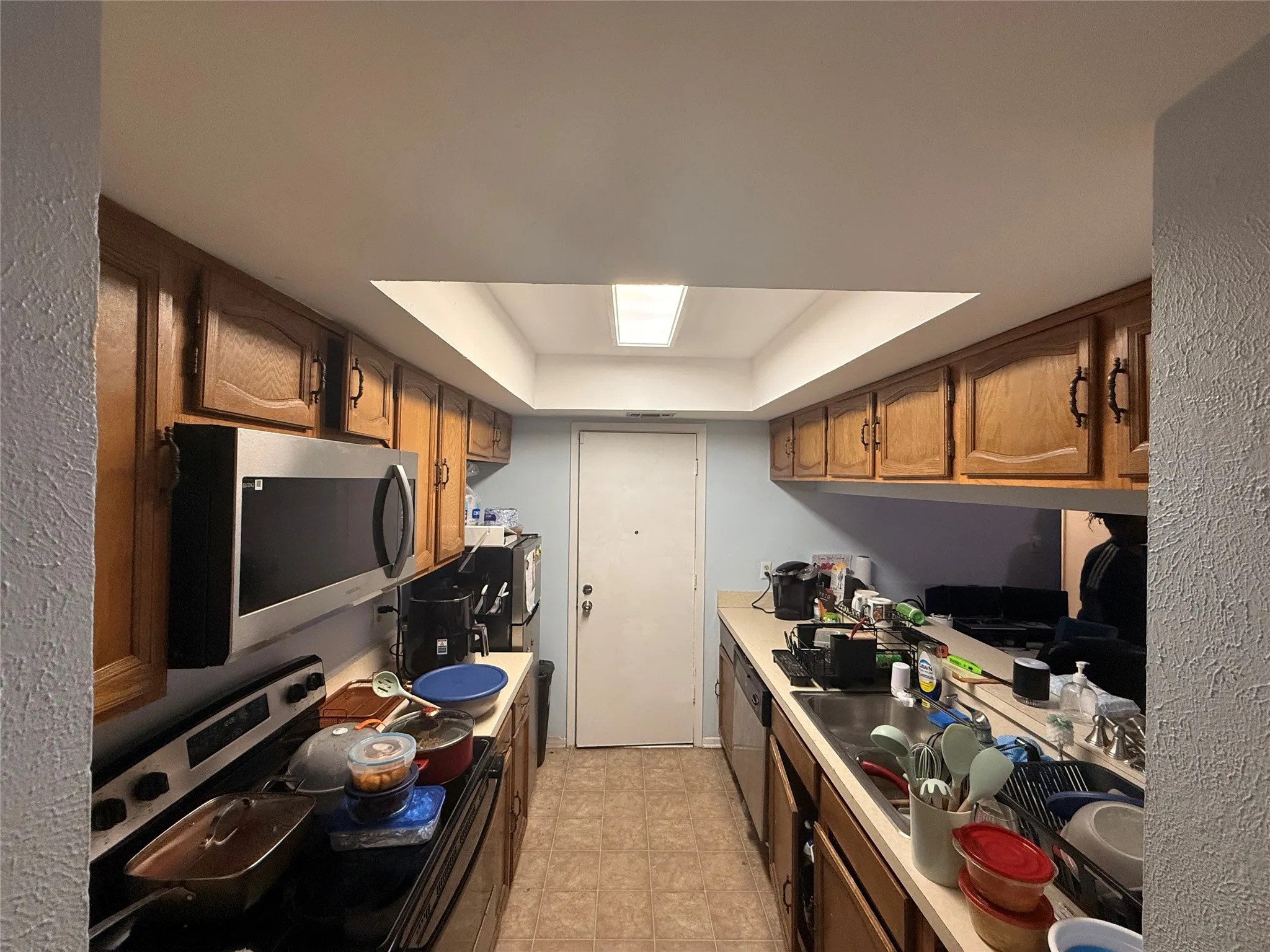 Galley kitchen featuring wood cabinetry, stainless steel microwave, electric range, and laminate countertops