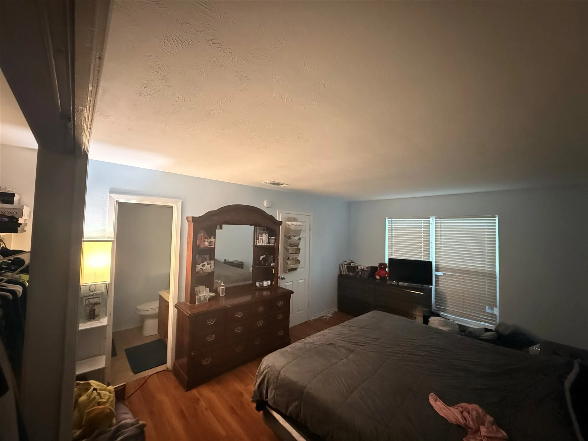 Room featuring light blue walls, wood-finish flooring, and a large window with horizontal blinds