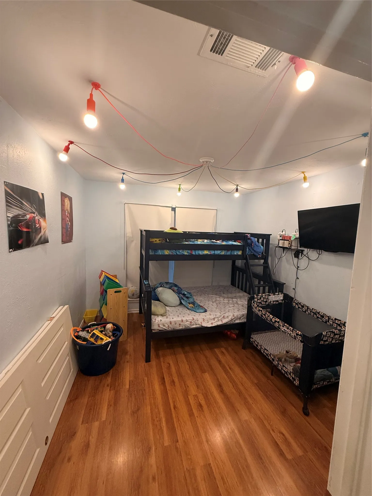 Room featuring wood-finish flooring, light blue wall paint, and a ceiling-mounted lighting fixture with exposed bulbs