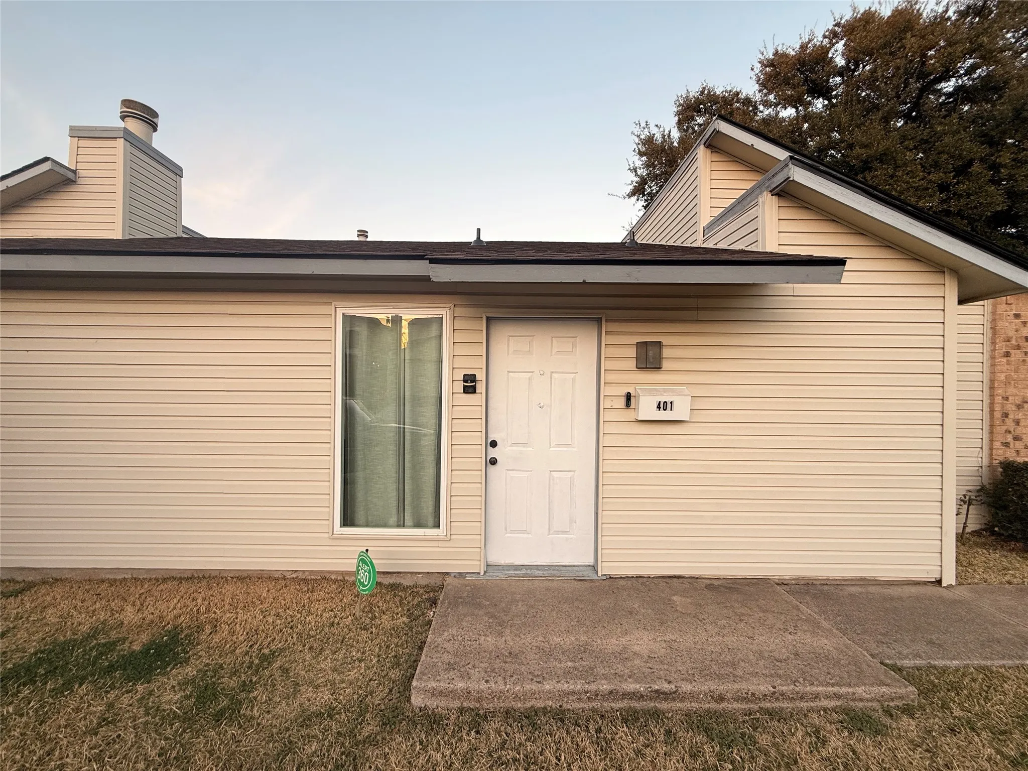 Cream-colored horizontal siding facade with a dark shingle roof and a prominent white entry door
