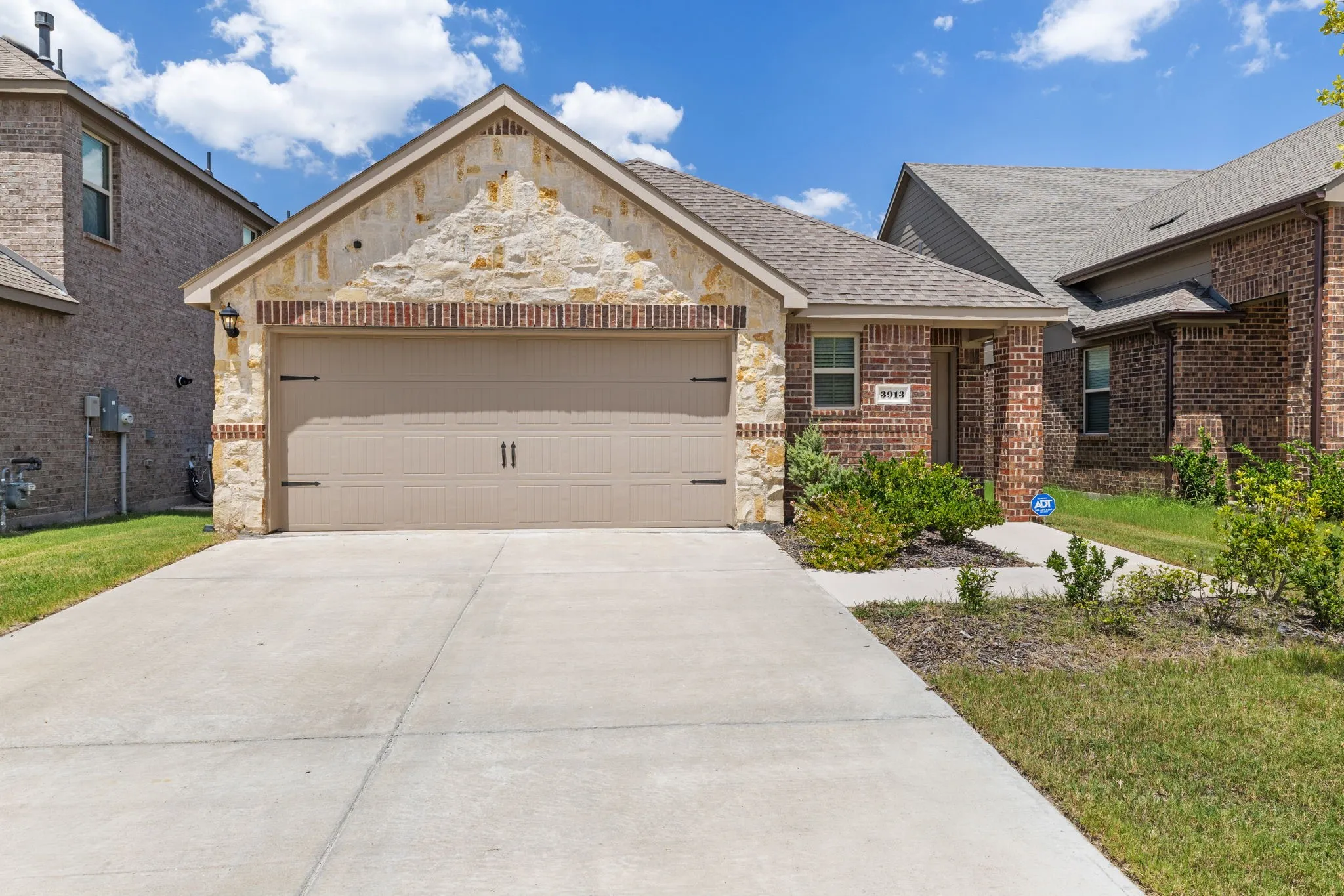 Exterior featuring a stone and brick facade, a single-door two-car garage, a concrete driveway, and mature landscaping.