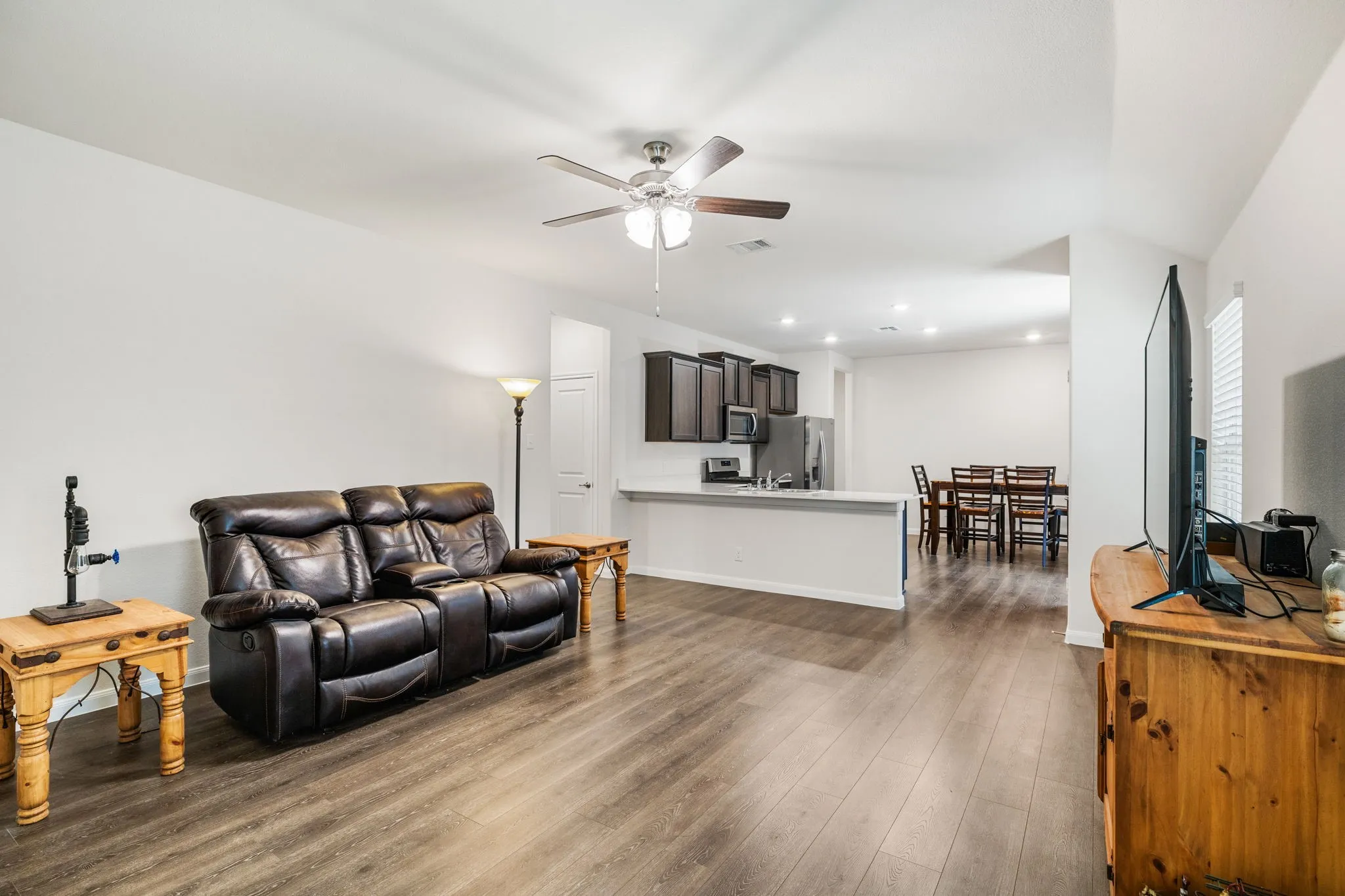 Open-concept living room looking toward kitchen, featuring luxury vinyl plank floors, a ceiling fan, and recessed lighting