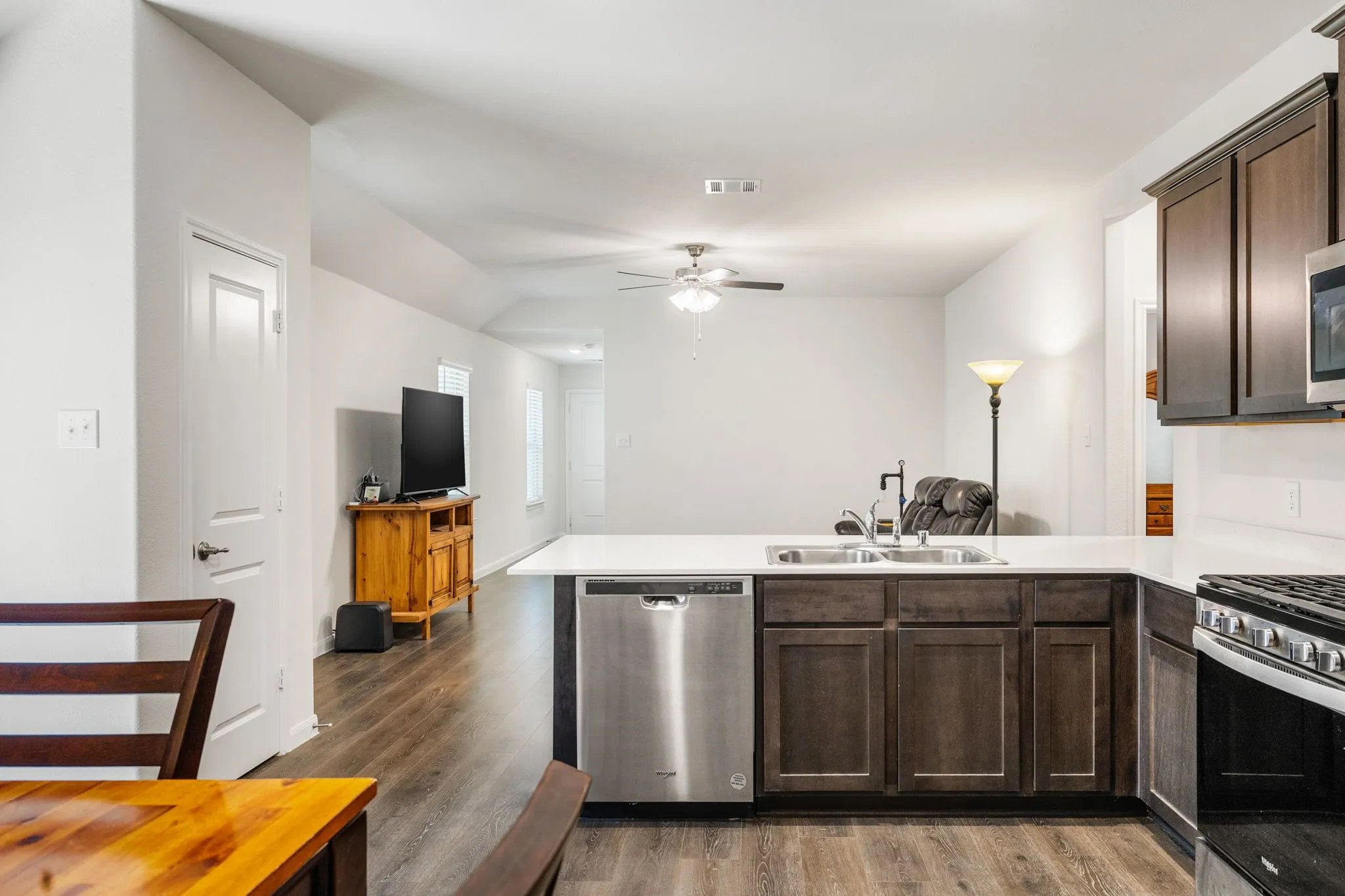 Open-concept kitchen and dining area with a peninsula counter top and breakfast bar plus gas range looking toward family room and front entry.