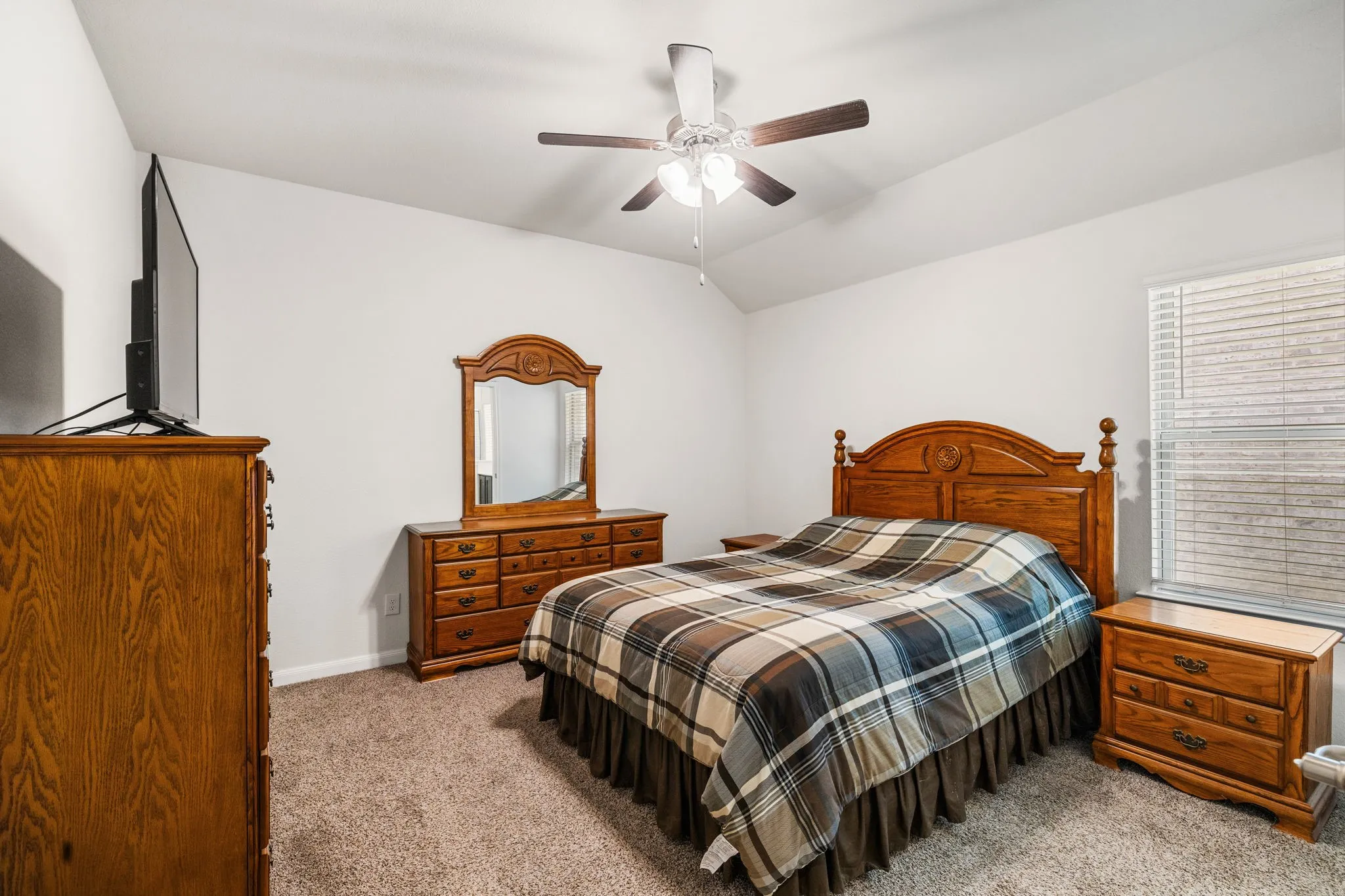 Primary bedroom featuring carpeted flooring, lofted ceiling, ensuite bath, and a ceiling fan