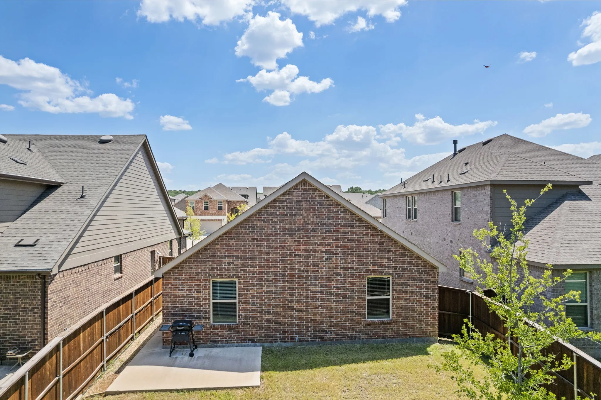 Aerial view of back of home surrounded by a brick exterior with a concrete patio area, a wood privacy fence.