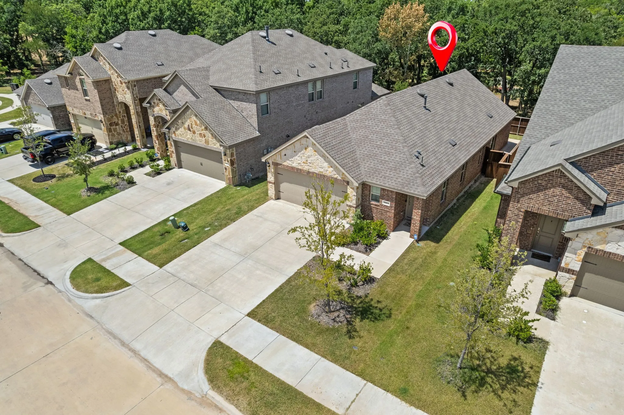 Aerial view of your next home at 3913 Nature Court. Brick and stone exterior with a two-car garage, concrete driveway, and a shingled roof.