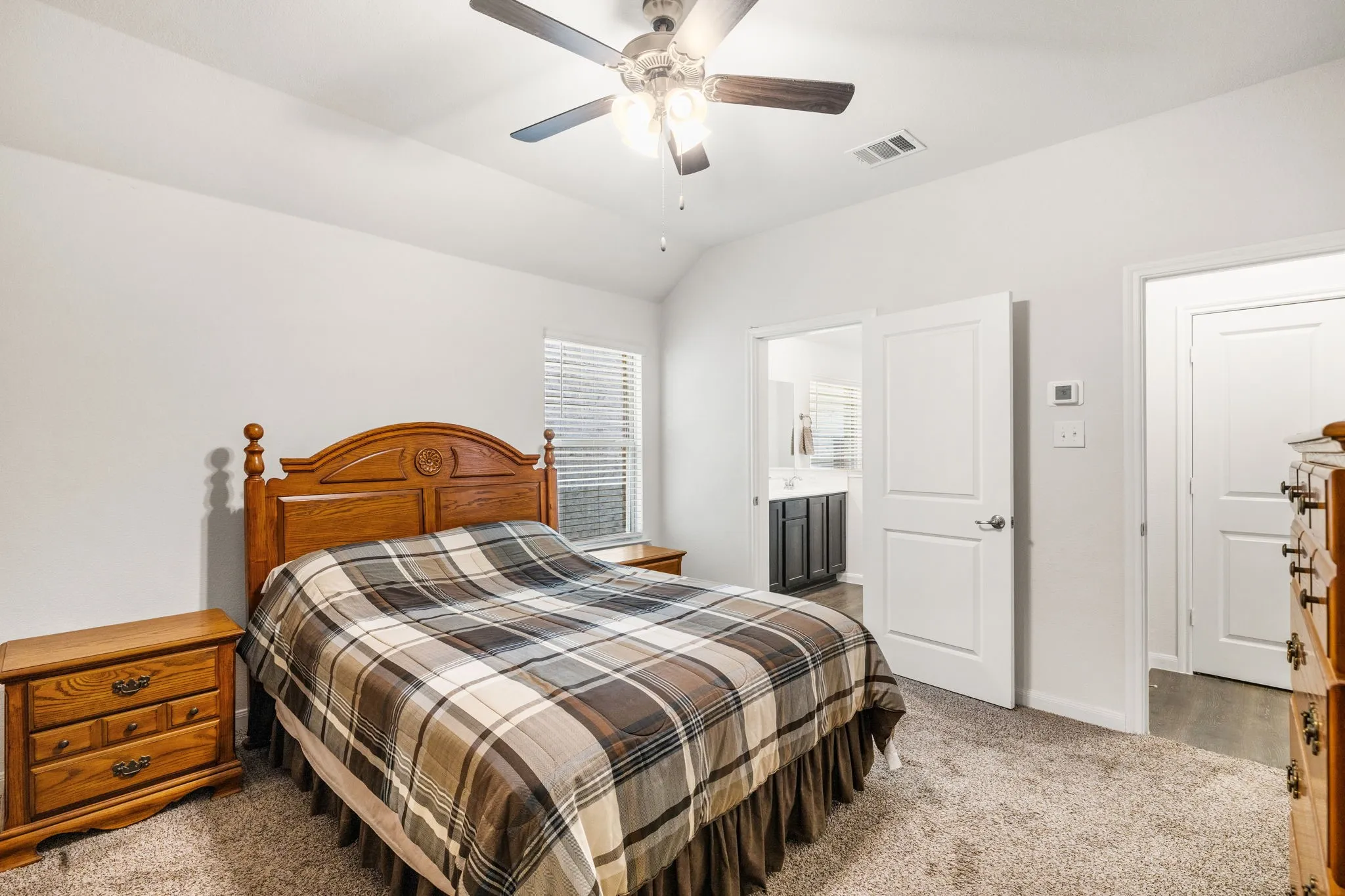 Primary bedroom featuring carpeted flooring, lofted ceiling, ensuite bath, and a ceiling fan