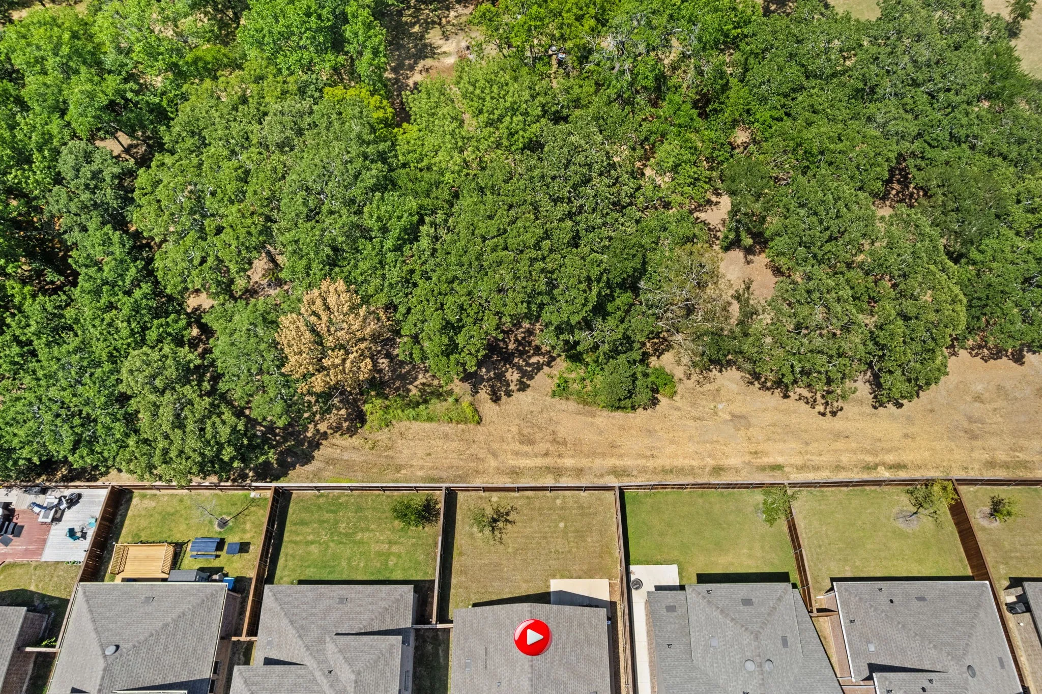 Aerial view of back of home showing spacious back yard with wood fence and treeline backdrop bordering the property