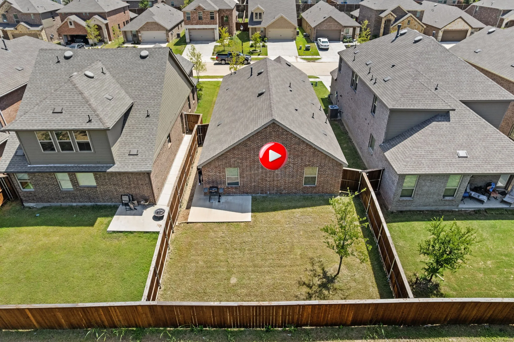 Aerial view of back of home with a patio area, an expansive fenced backyard, brick siding, and a residential view.