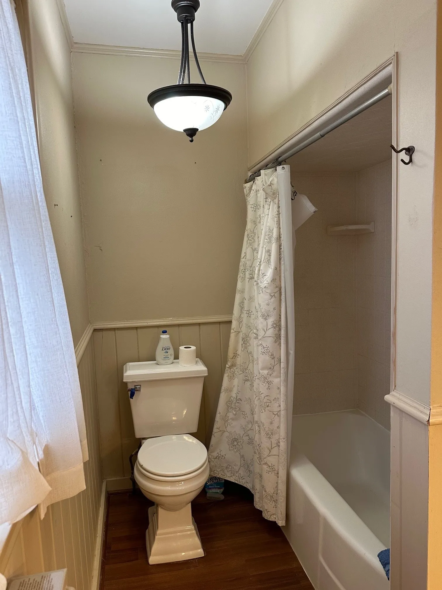 Full bathroom with a tub/shower combination, white toilet, wood-finish flooring, and​​‌​​​​‌​​‌‌​‌‌​​​‌‌​‌​‌​‌​​​‌​​ wainscoting