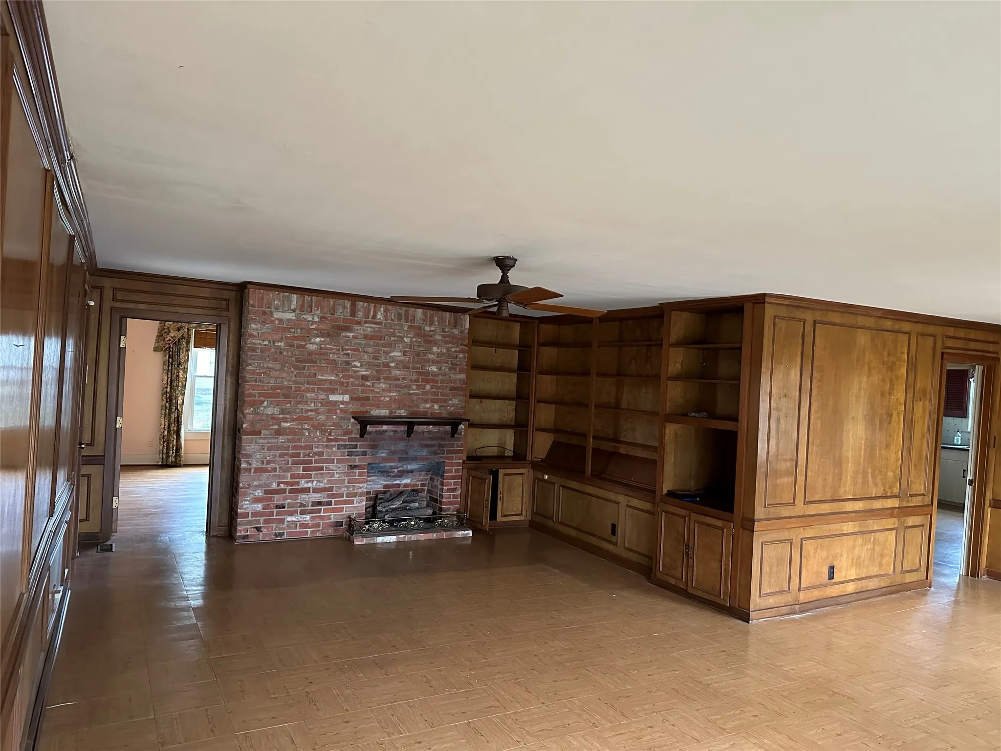 Spacious interior featuring a brick fireplace, built-in shelving, extensive wood paneling, and a ceiling fan