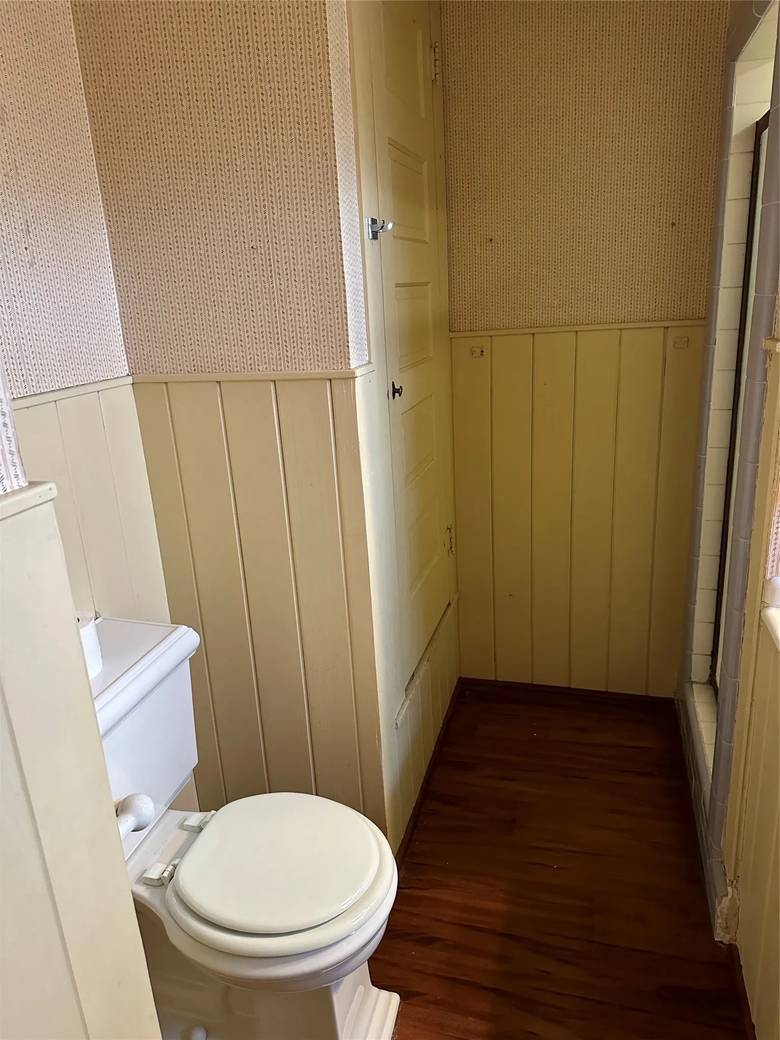 Bathroom with wood-finish flooring, wainscoting, and a white toilet