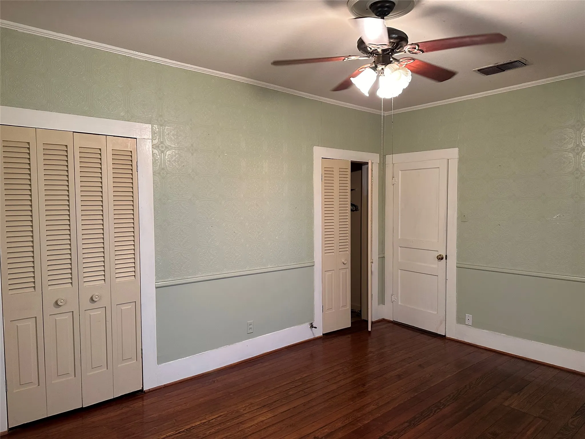Hardwood flooring throughout featuring a ceiling fan with integrated lighting, bi-fold louvered closet doors, and crown molding