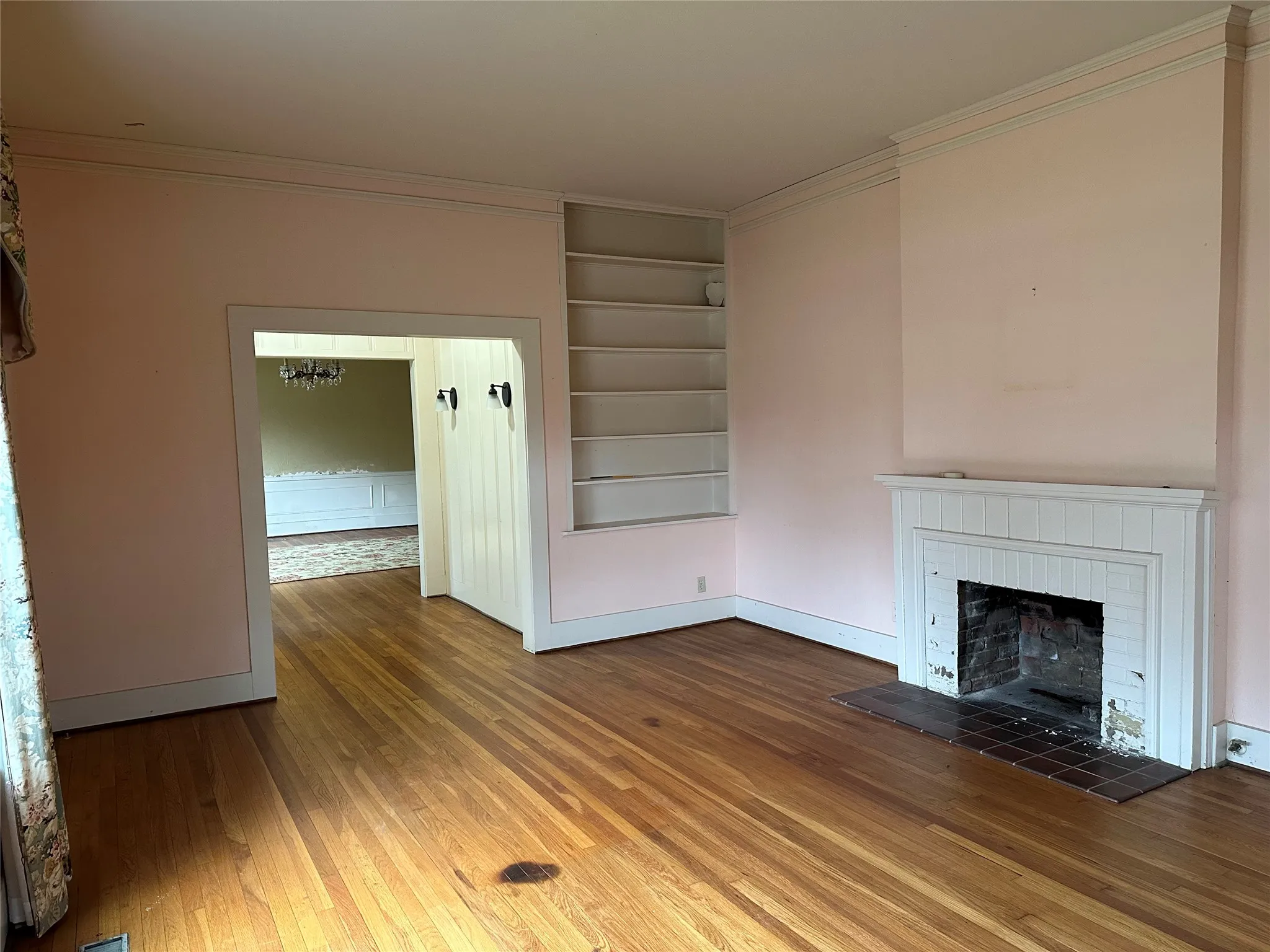 Living area featuring wood-finish flooring, a white tiled fireplace surround, an integrated bookshelf, and crown molding