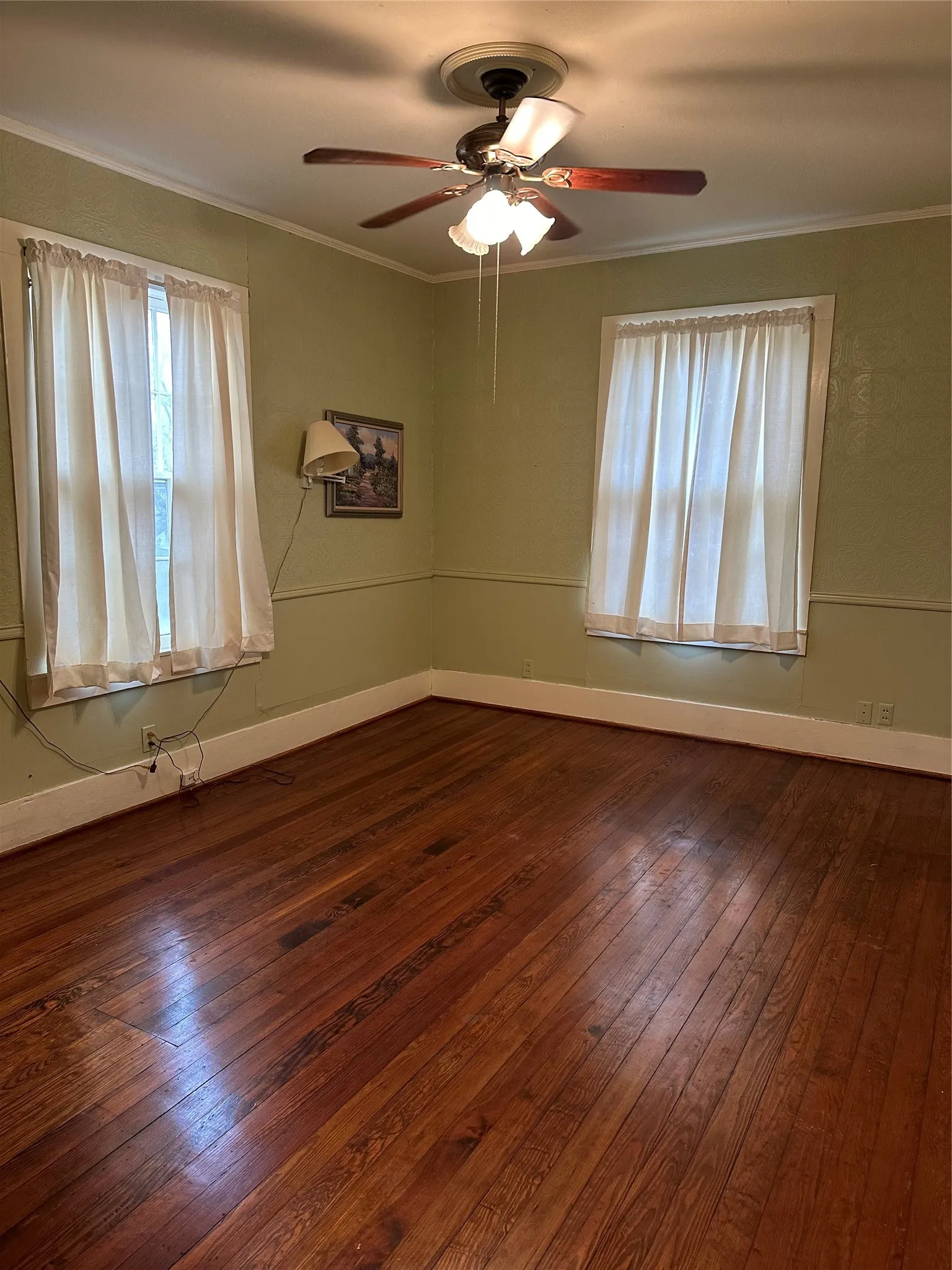 Room featuring wood-finish flooring, two window openings, a ceiling fan with integrated lighting, and crown molding
