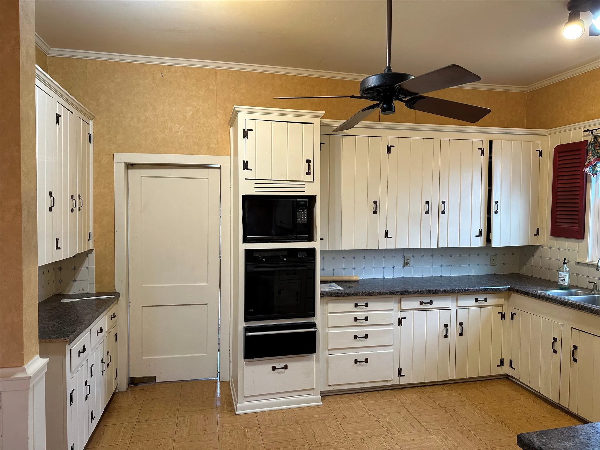 Kitchen featuring extensive white cabinetry with black hardware, built-in microwave and oven, dark countertops, and patterned wallpaper