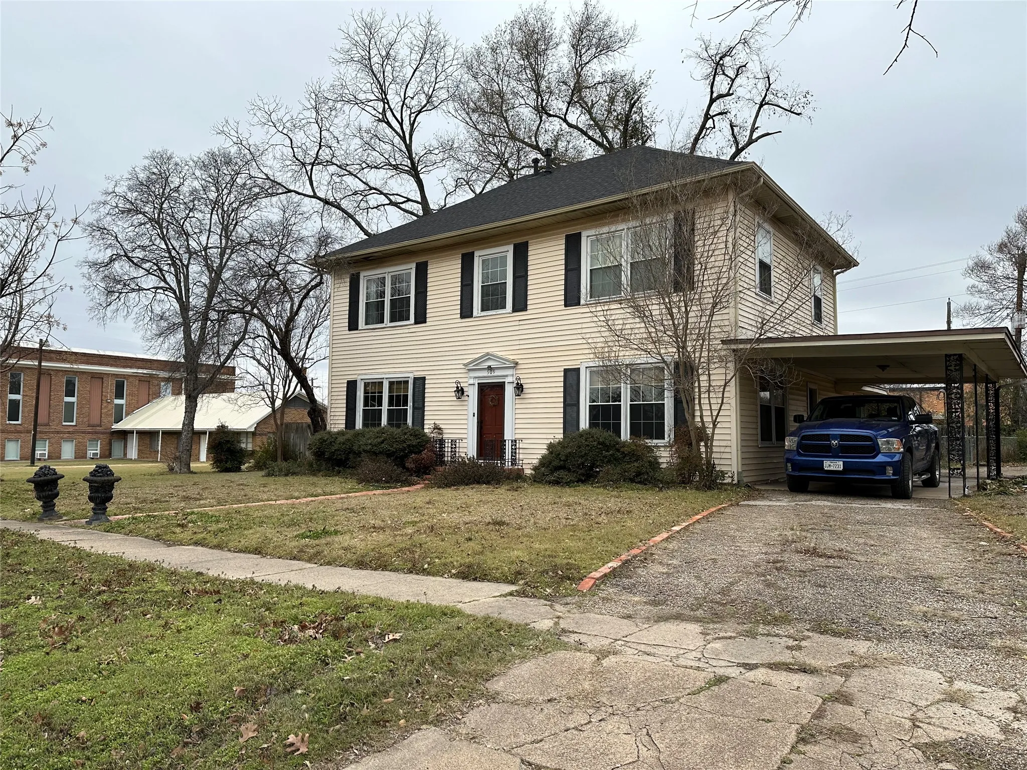 Two-story residence featuring light-colored siding, dark shutters, a covered entry porch, and a dedicated carport