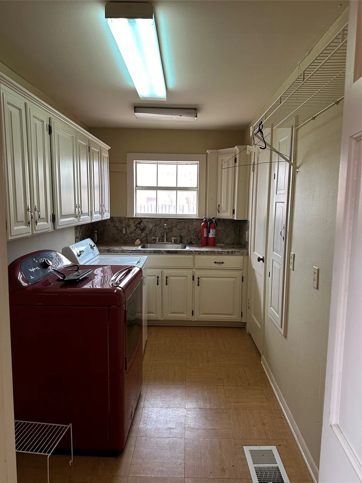 Laundry area featuring white cabinetry, a utility sink with a window, tile-look flooring, and overhead fluorescent lighting