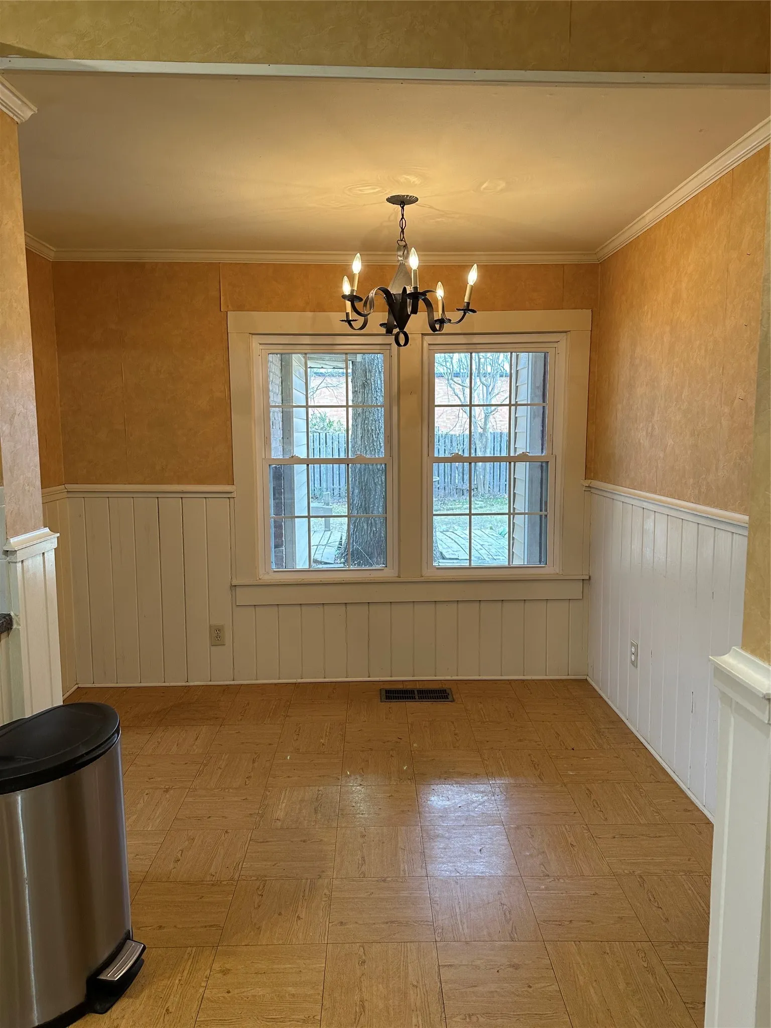Dining area in Kitchen featuring two large windows, a chandelier light fixture, crown molding, and wainscoting