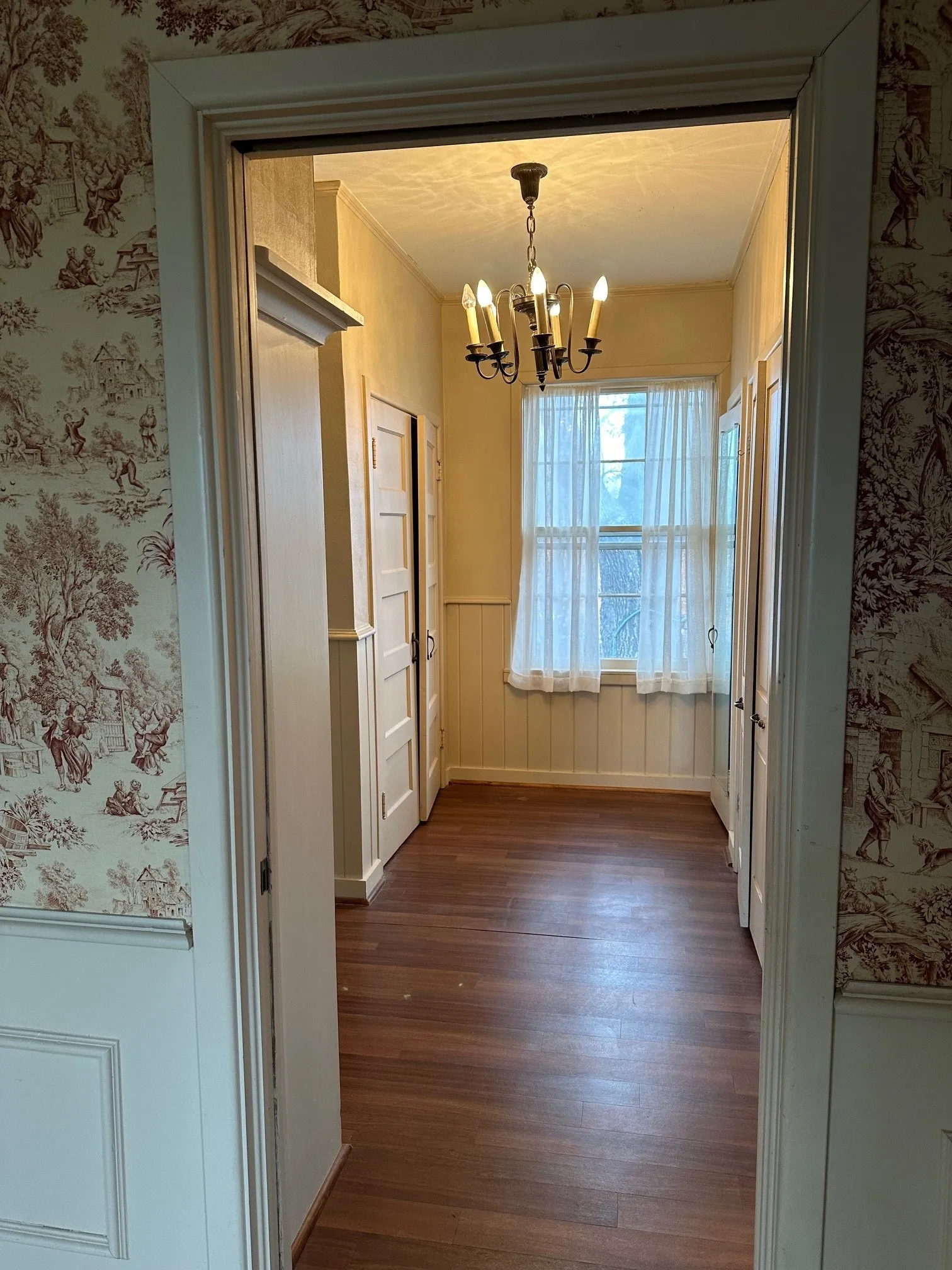 Hallway featuring wood-finish flooring, a central chandelier, multiple paneled doors, and wainscoting
