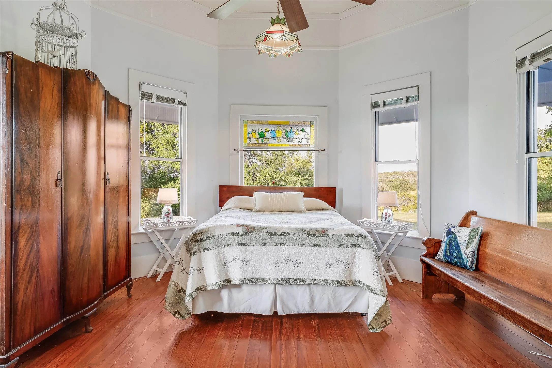 Hardwood flooring complements a bright room featuring multiple windows, a ceiling fan, and a stained-glass transom
