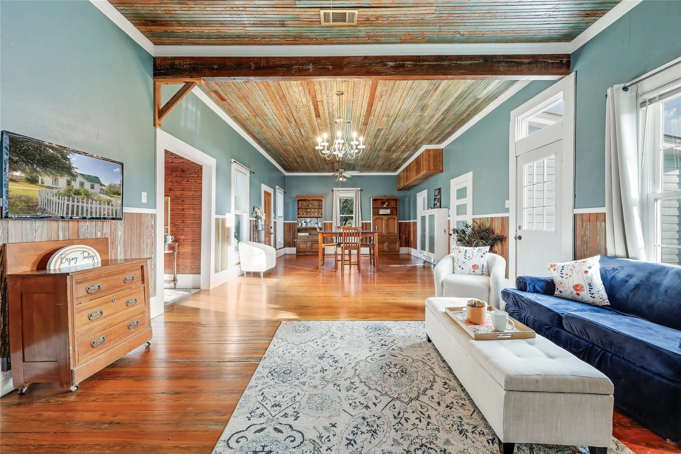 Open-concept living area featuring a wood-finish ceiling, exposed structural beams, wood-finish flooring, and wainscoting