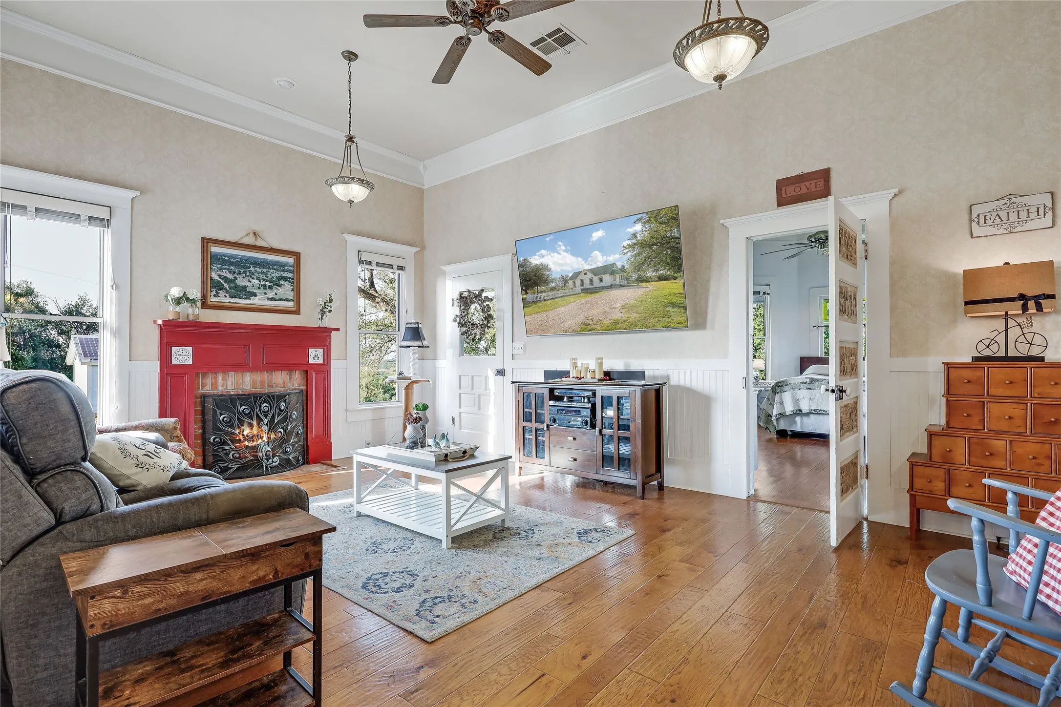 Living area featuring wood-finish flooring, a red mantel with a brick fireplace, and white wainscoting