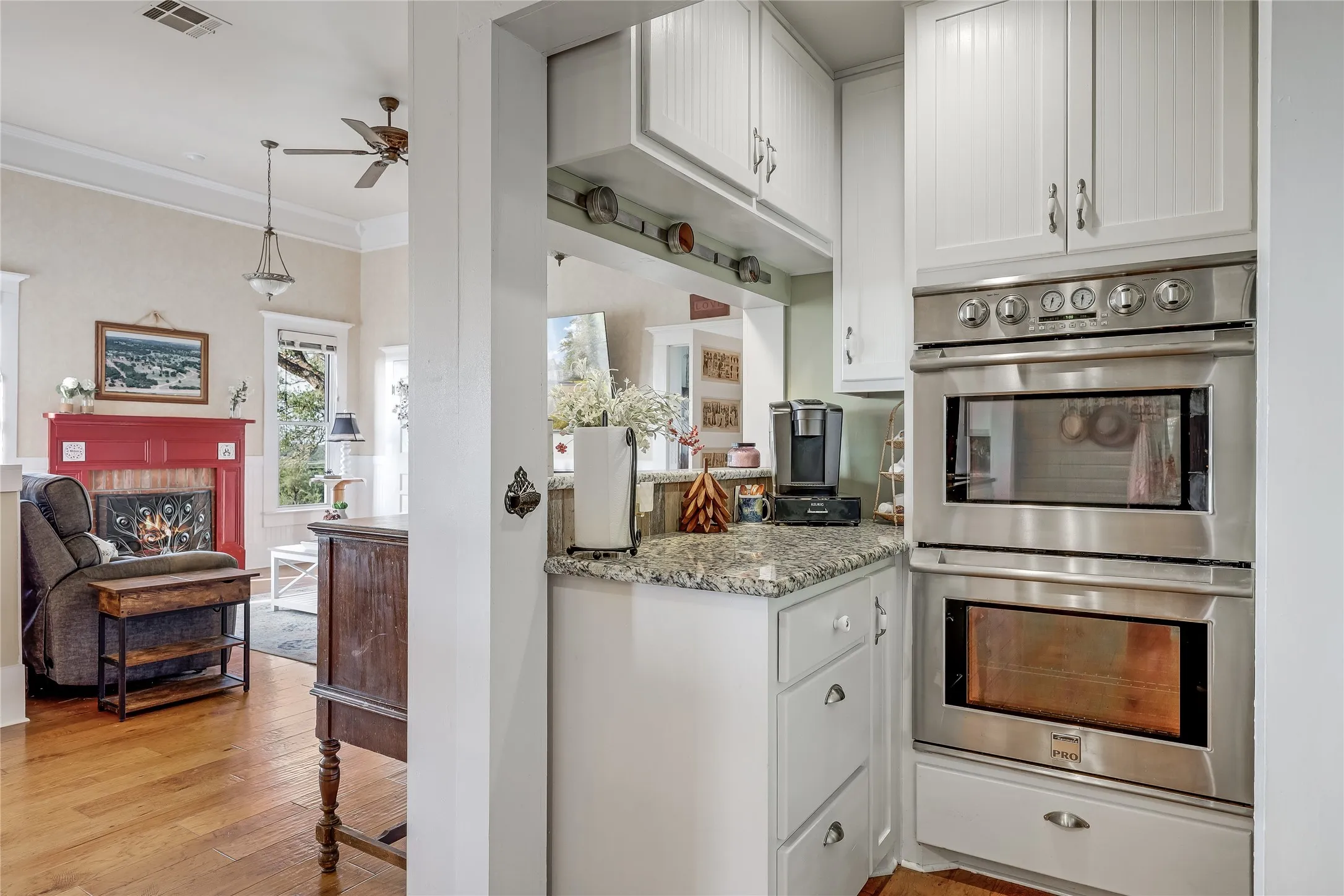 White cabinetry featuring beadboard detailing, stainless steel double wall ovens, granite-finish countertop, and wood-finish flooring