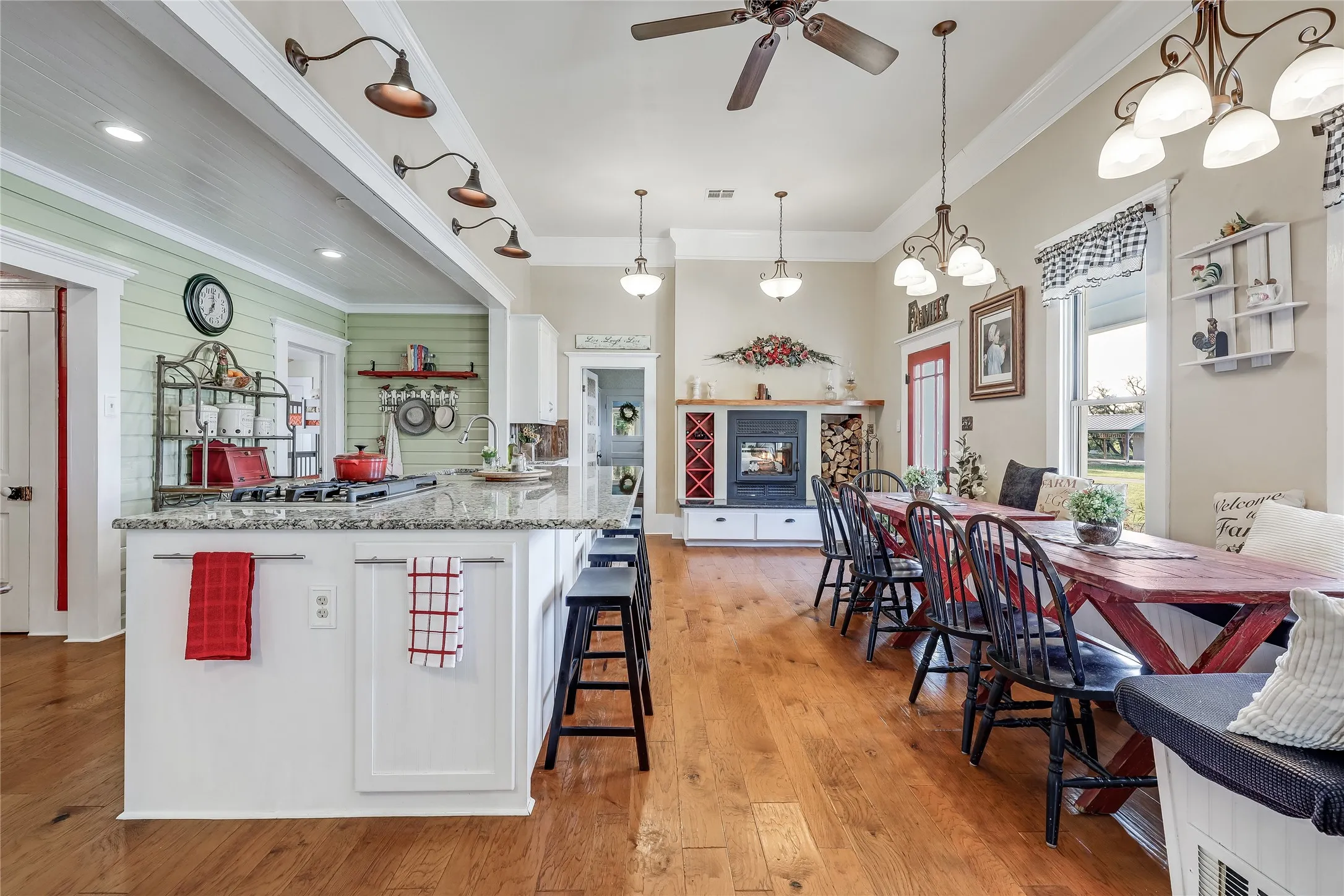 Open-concept living area with wood-finish flooring, a kitchen island featuring a granite countertop, a built-in fireplace with log storage, and pendant lighting throughout