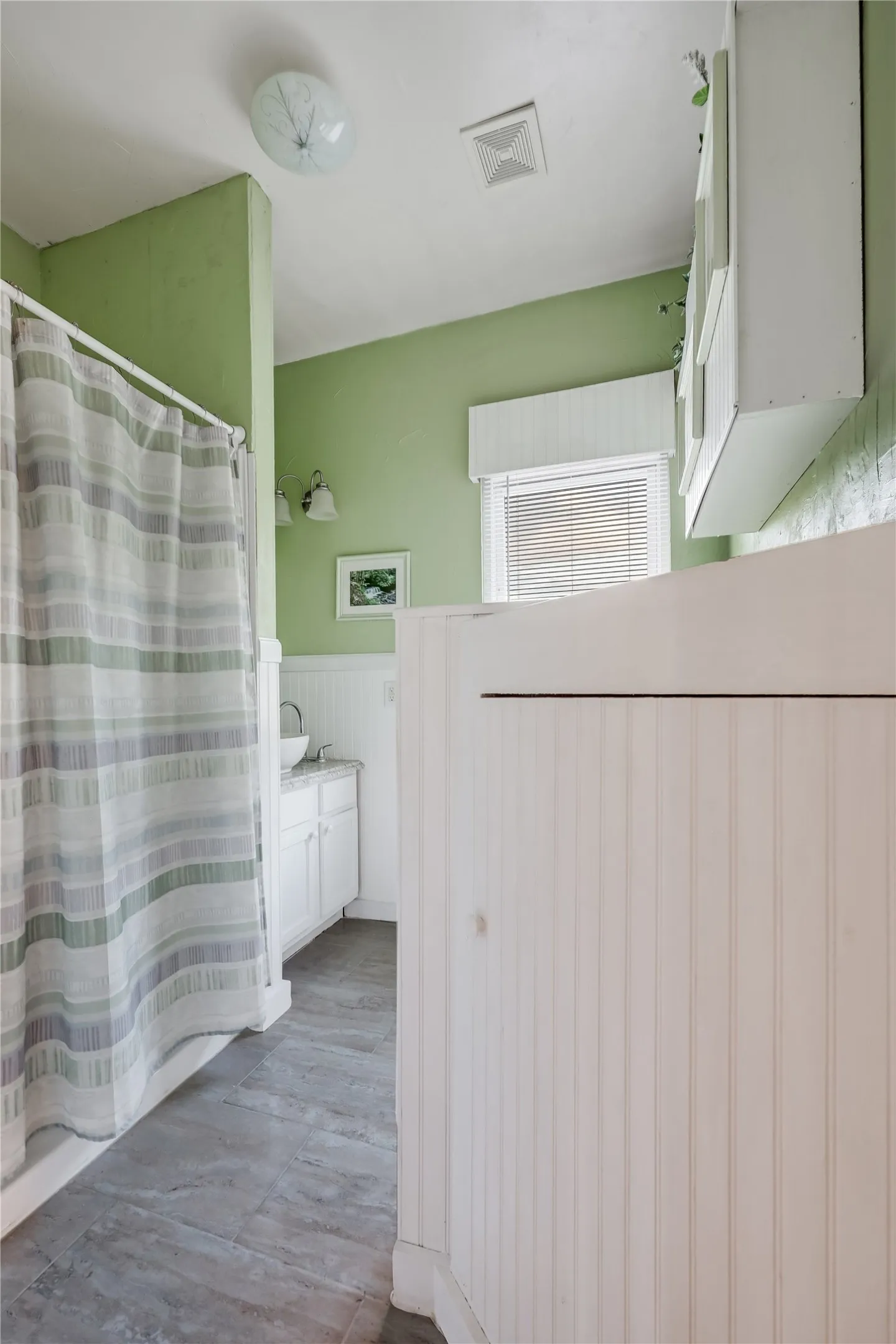 Bathroom featuring grey tile flooring, white beadboard wainscoting, and a white vanity with an undermount sink