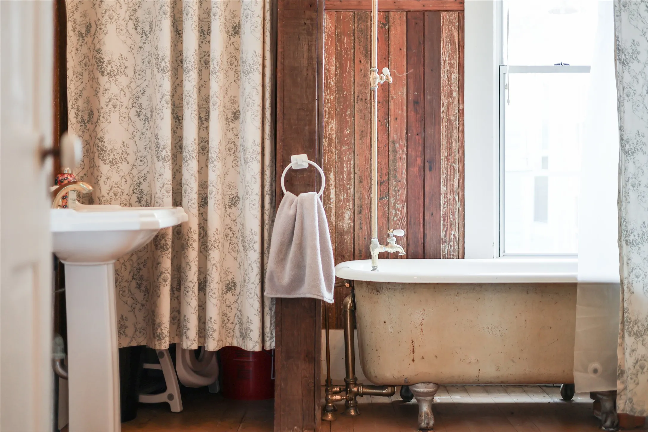 Vintage clawfoot bathtub with exposed plumbing, set against distressed wood paneling