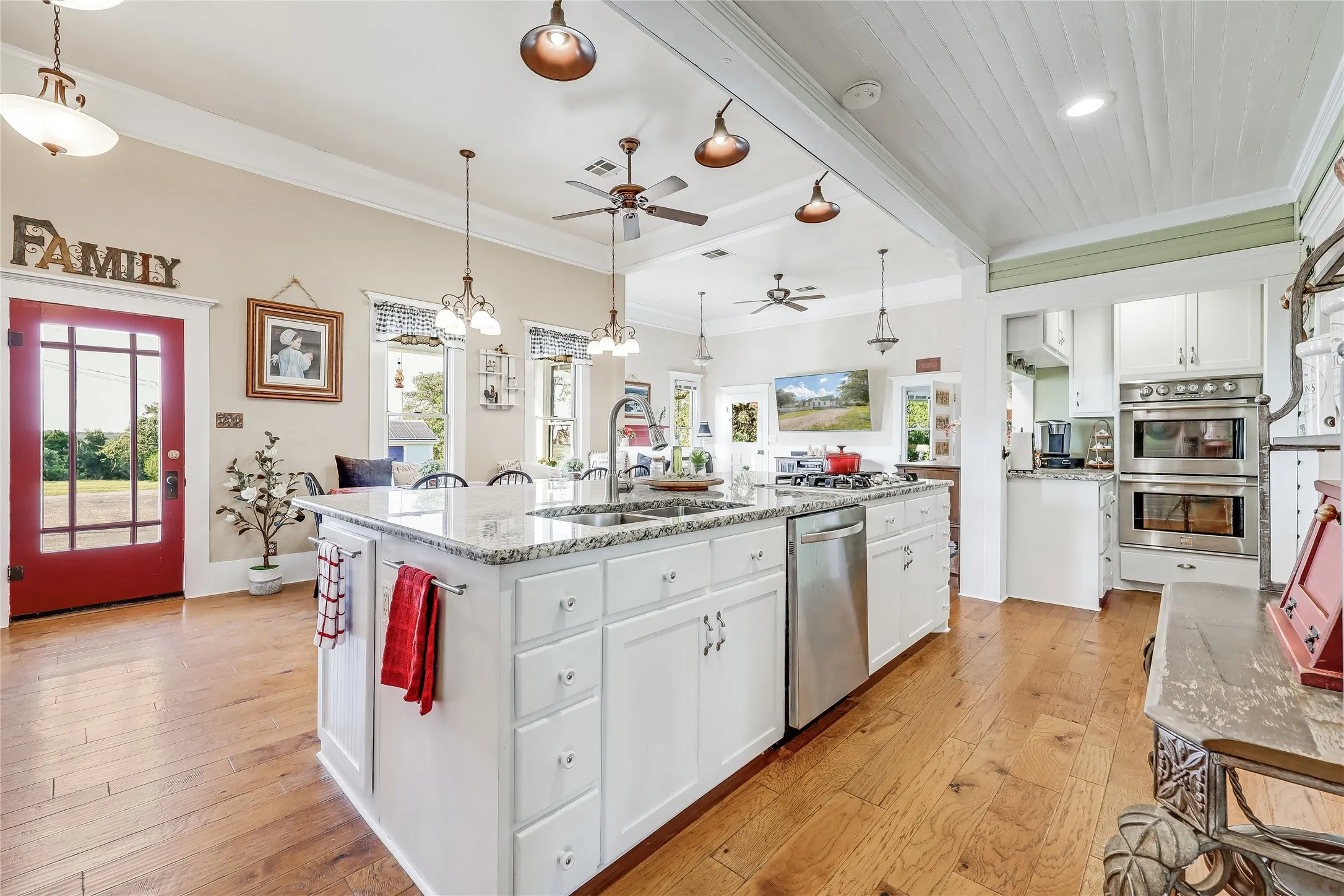 Spacious kitchen featuring a large central island with granite countertop, white cabinetry, integrated stainless steel appliances, and wood-finish flooring throughout