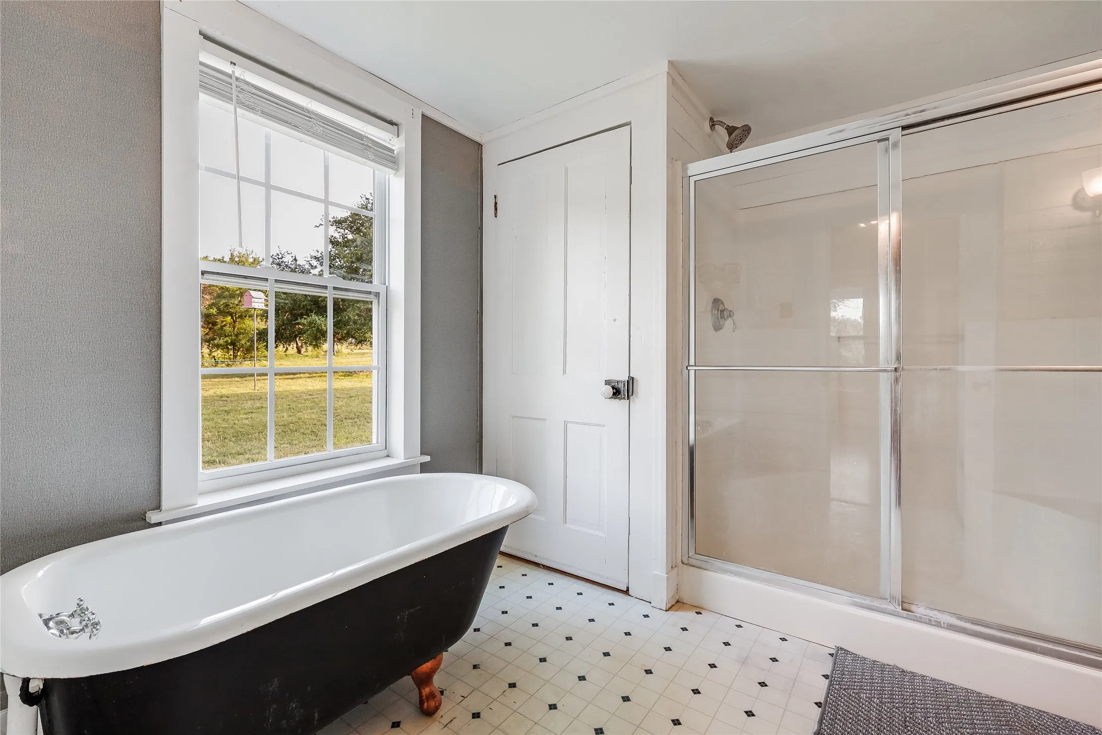 Clawfoot tub and separate glass-enclosed shower featuring a tiled floor, white trim, and a window with outdoor scenery