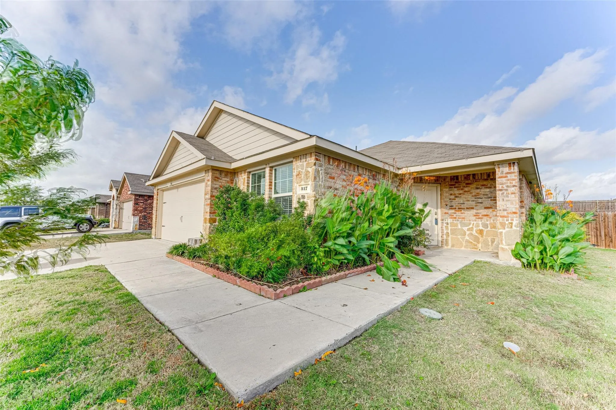 Single-story residence featuring a two-car garage, stone and siding exterior, concrete driveway, front yard with mature landscaping, and a covered entry porch