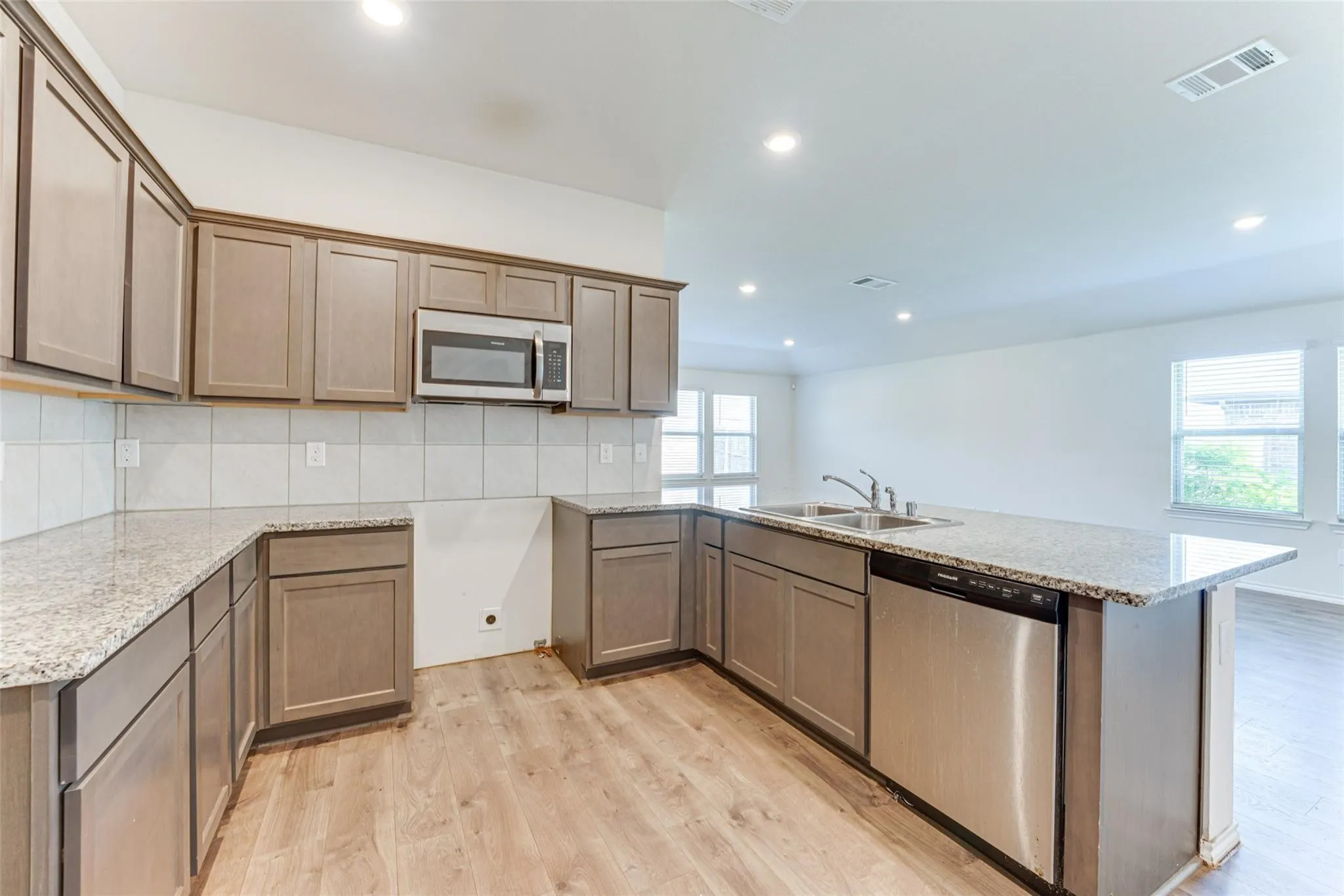 Kitchen featuring wood-finish flooring, granite countertops, gray cabinetry, white subway tile backsplash, and stainless steel appliances including a microwave and dishwasher