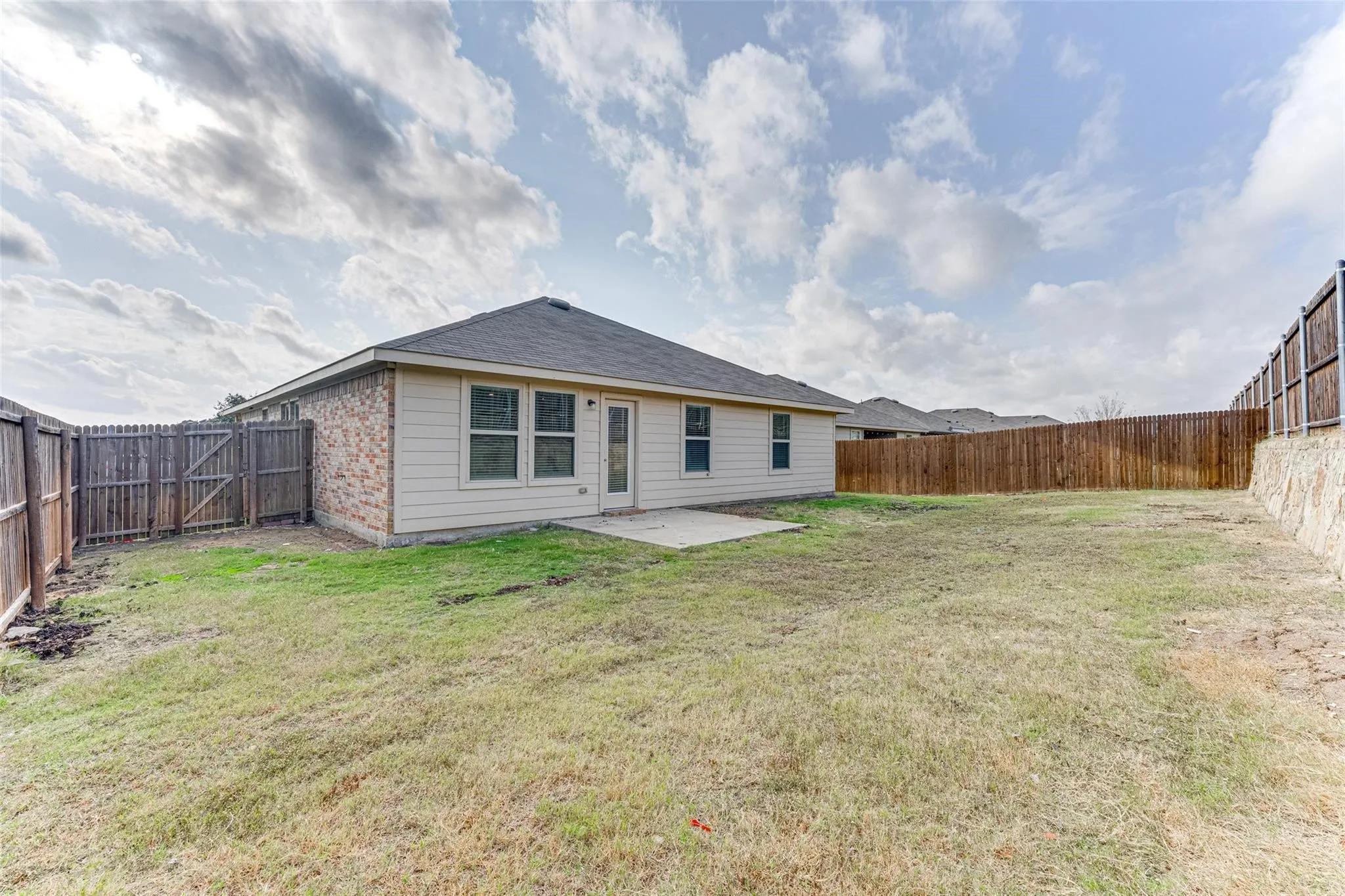 Expansive backyard featuring a privacy fence, concrete patio, and a stone retaining wall