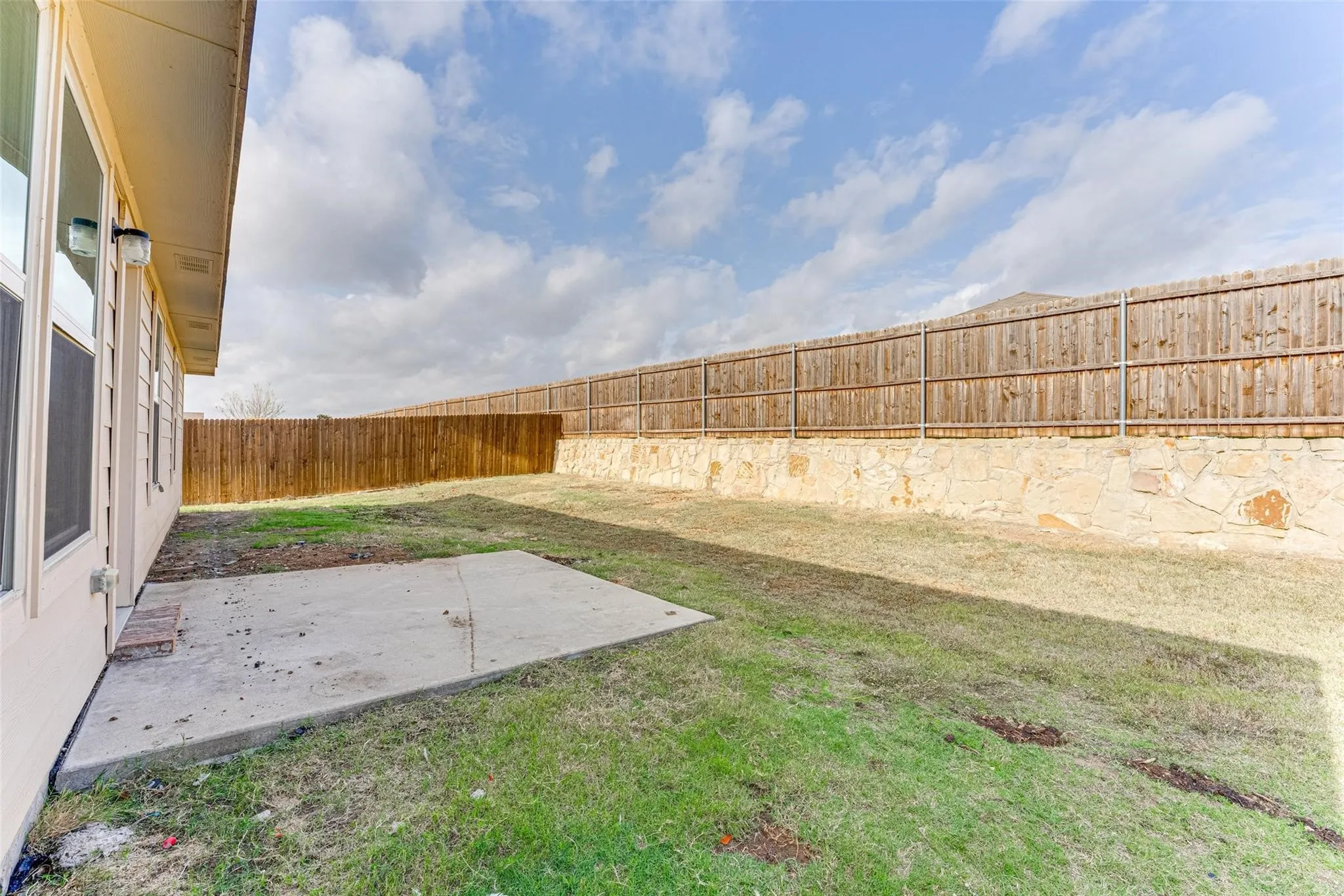 Expansive grassy yard featuring a concrete patio, a wood privacy fence, and a stone retaining wall