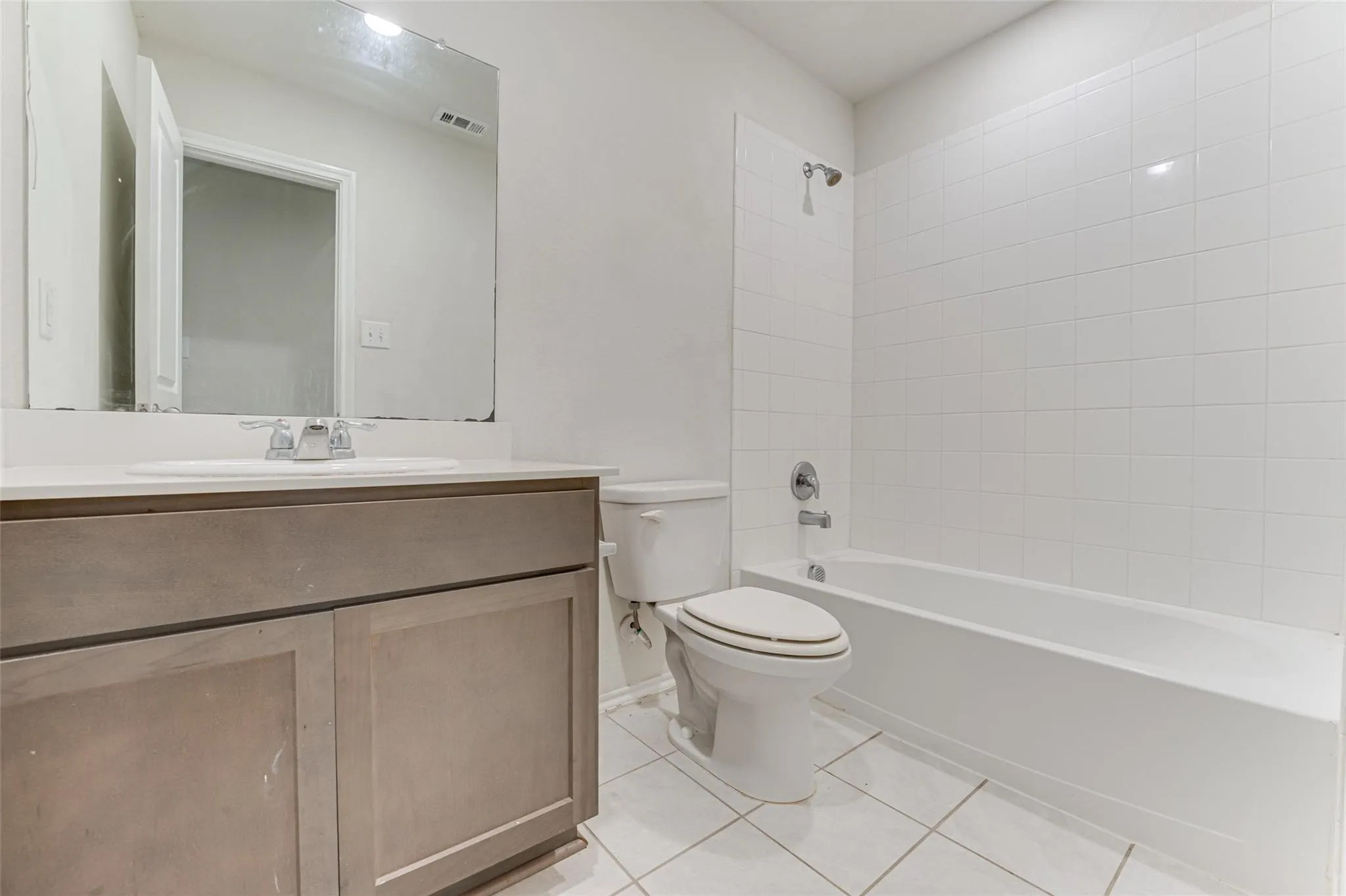 Bathroom featuring a vanity with a white countertop and undermount sink, a large wall-mounted mirror, a commode, and a tub-shower combination with white subway tile surround