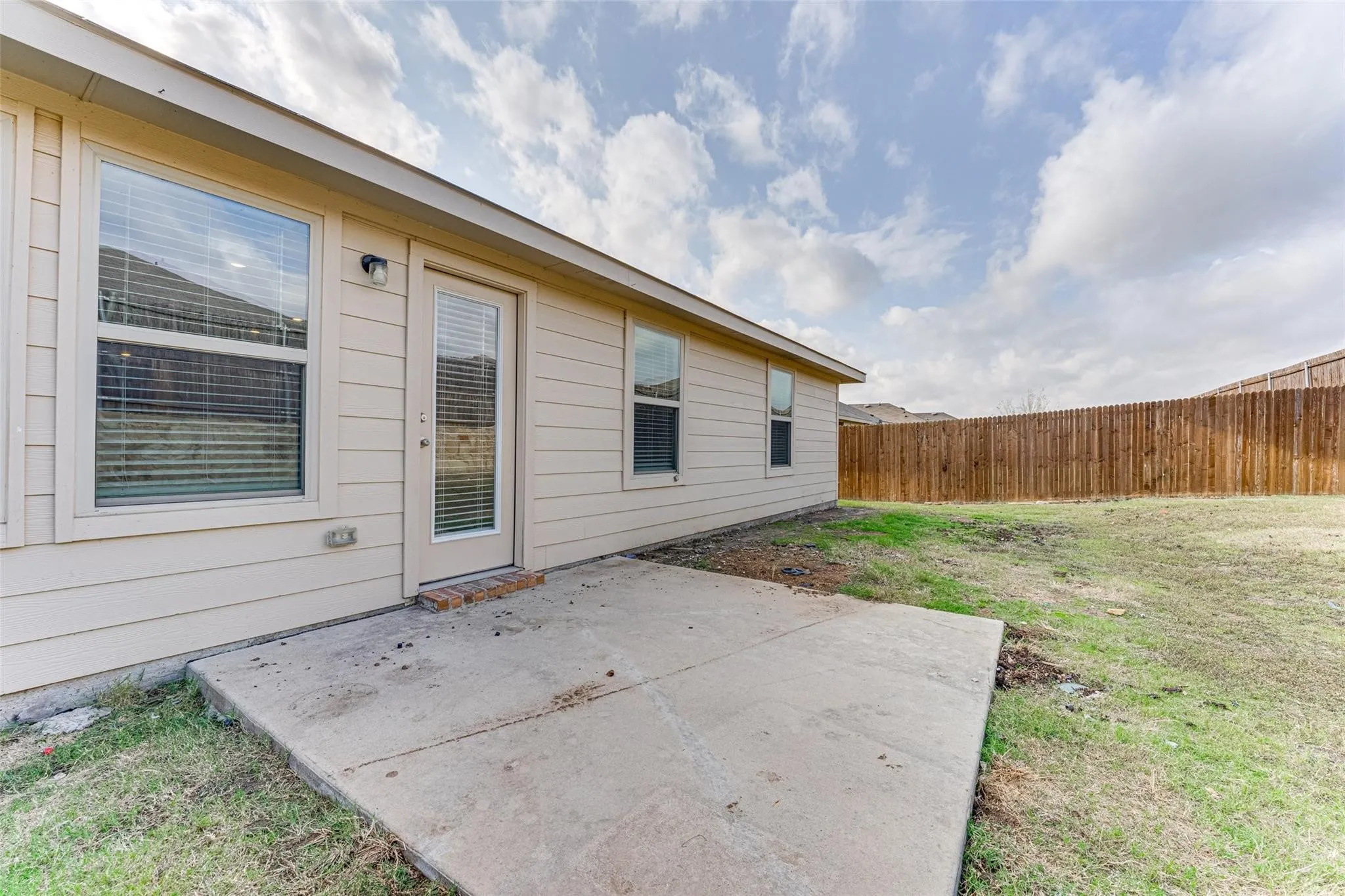 Expansive backyard featuring a concrete patio, wood privacy fence, and beige exterior siding