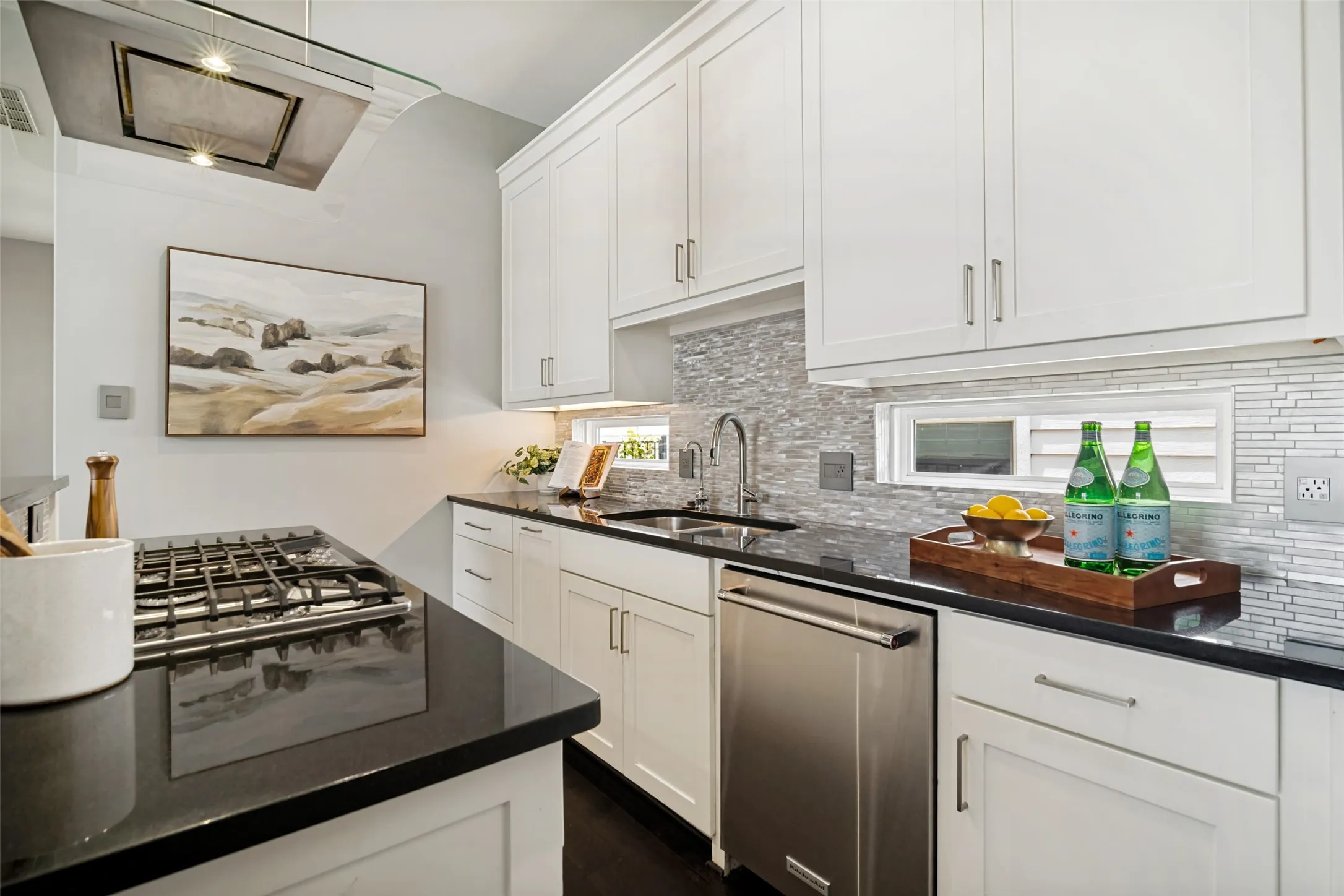Light-filled kitchen with rectangular windows, island with breakfast bar, commercial-style vent hood, white stone backsplash, and spacious walk-in pantry.